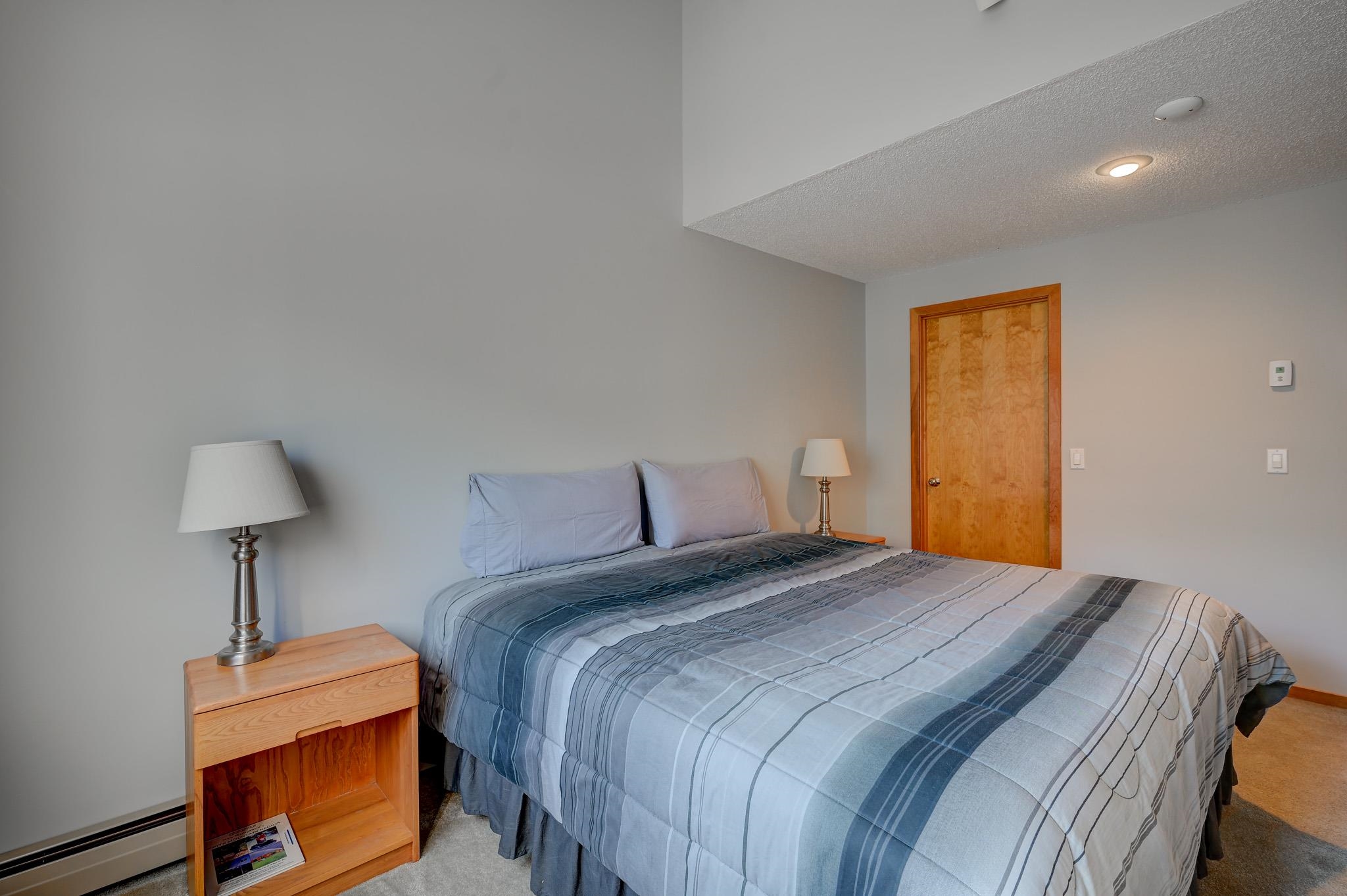 Bedroom with a large blue-gray striped bedspread and wooden nightstands.