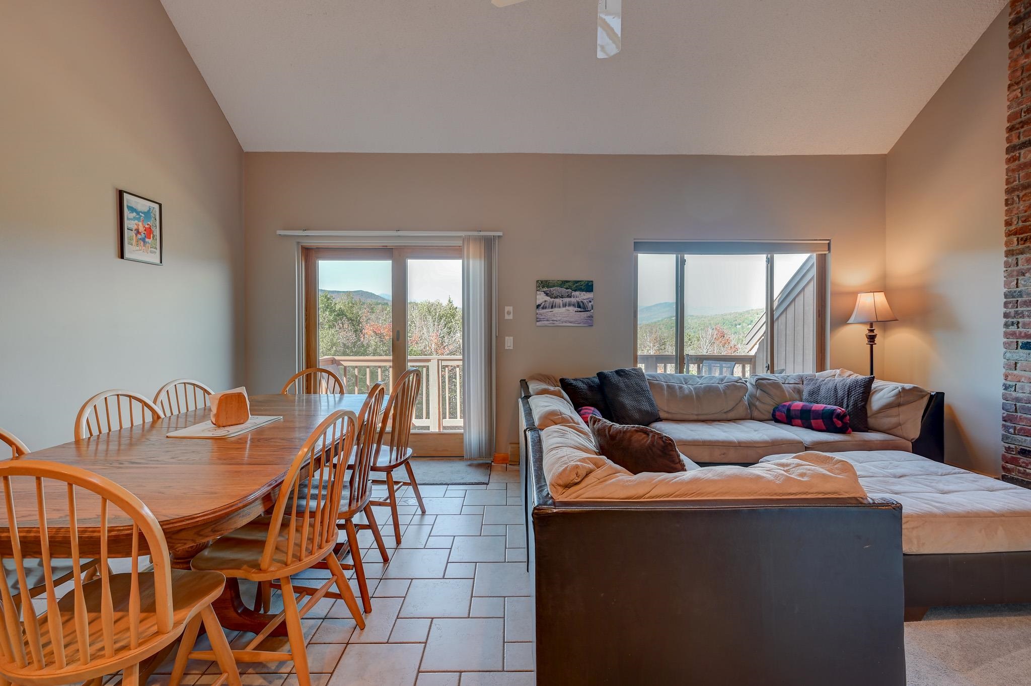 Open-plan living and dining area with a wood table, sectional sofa, and mountain views through sliding doors.