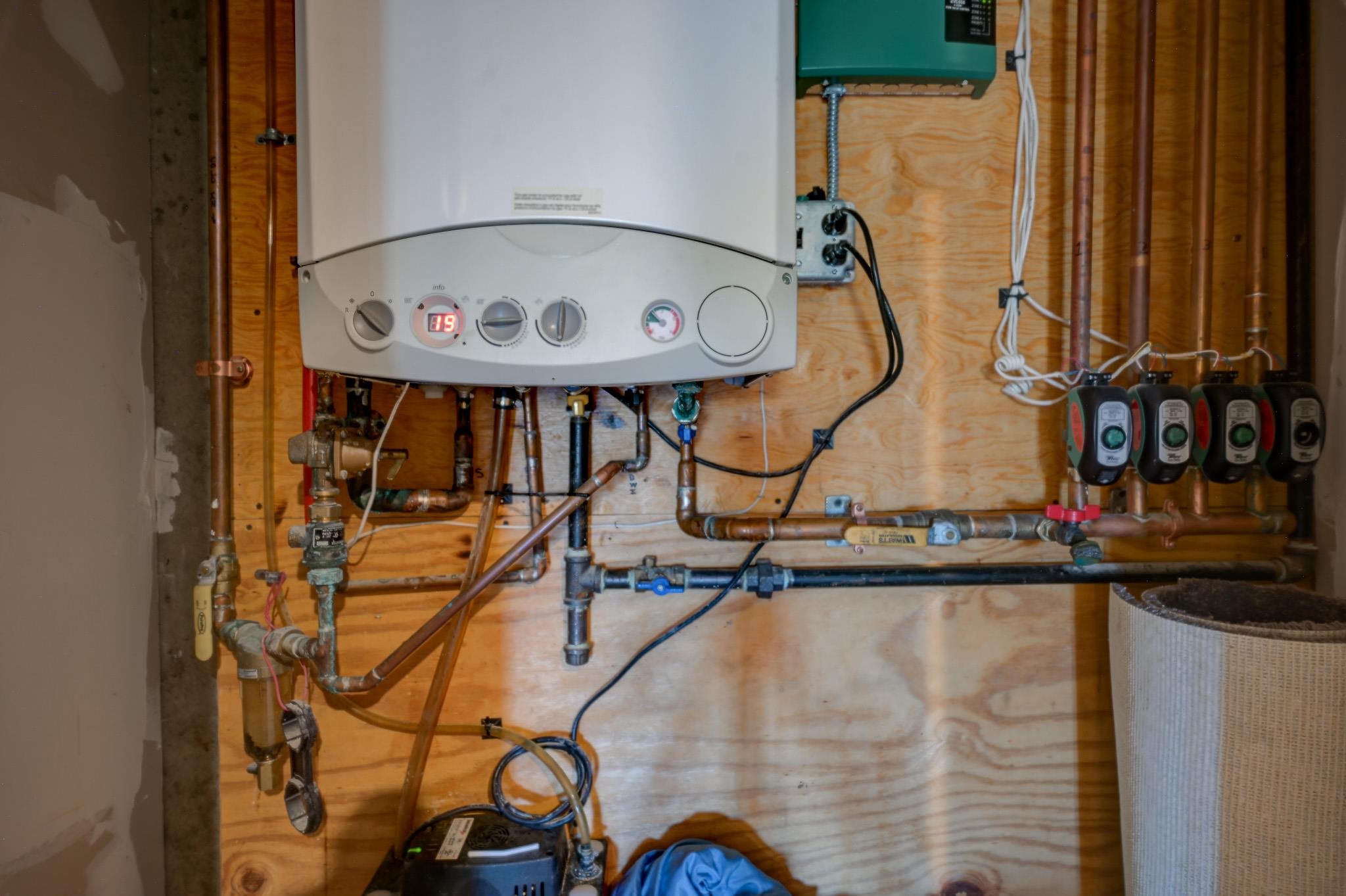 Mechanical room with a wall-mounted boiler, exposed piping, and heating circulation pumps.