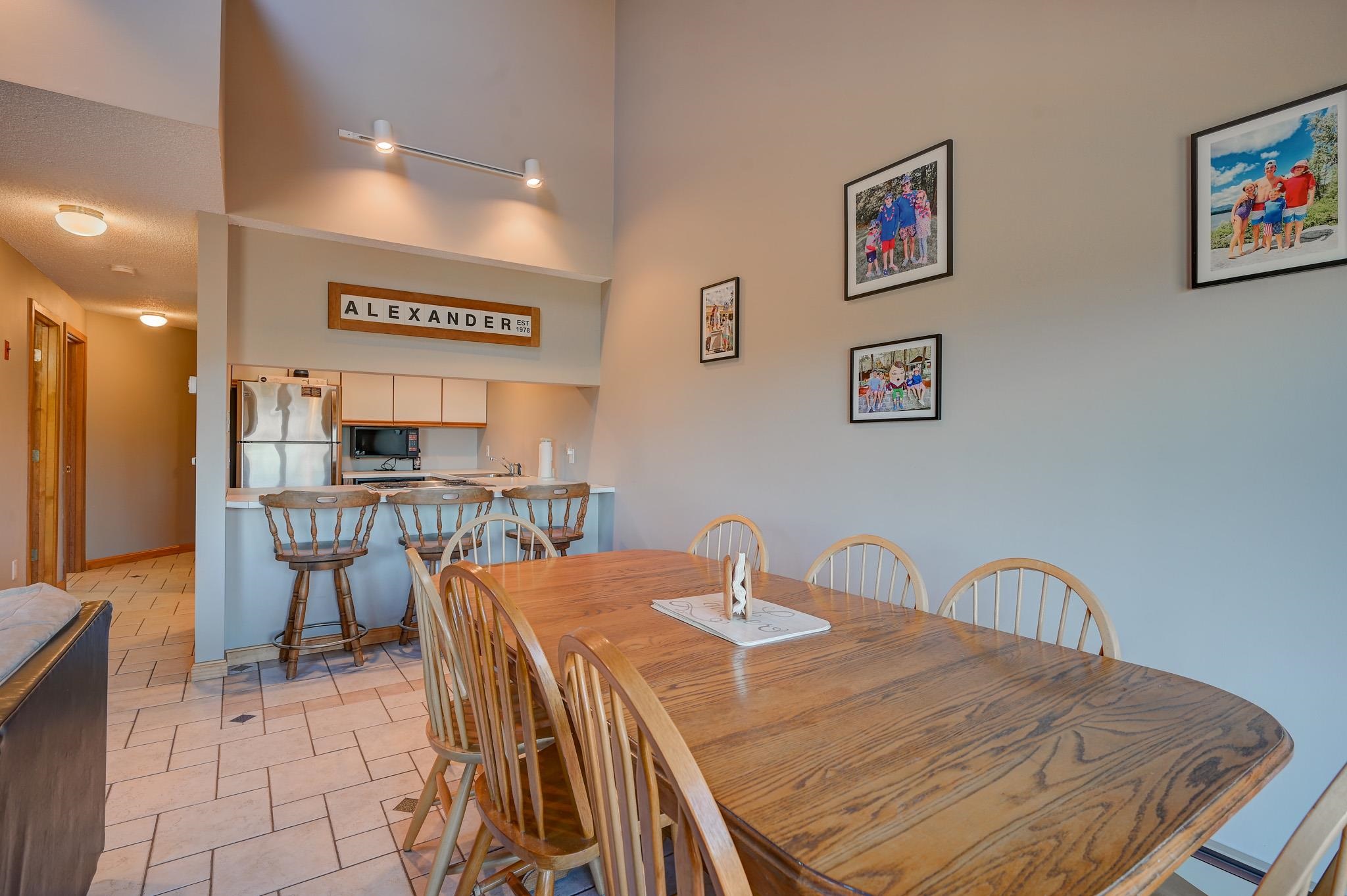 Dining area with a long wooden table and chairs beside a kitchen breakfast bar.