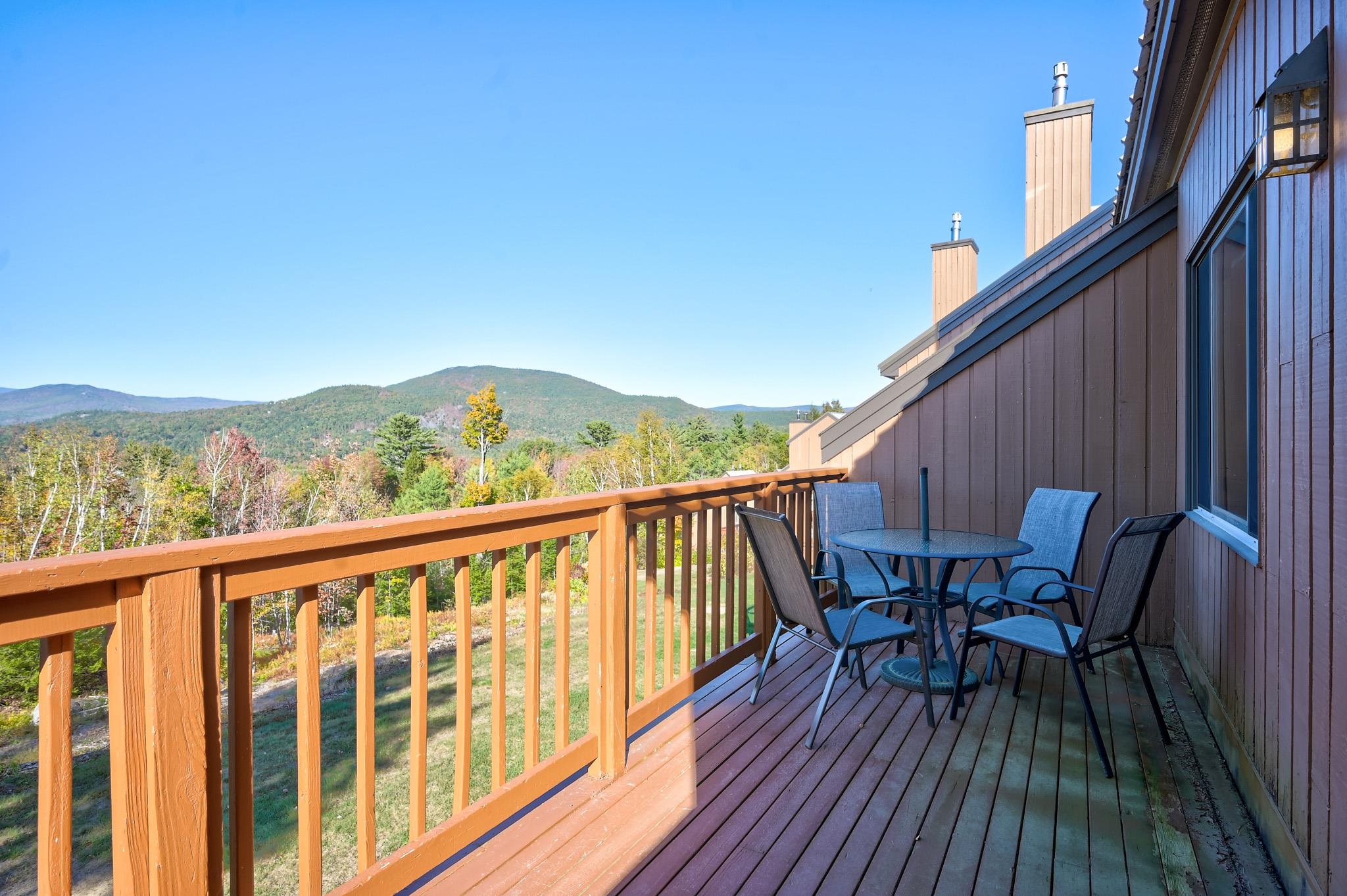 Furnished wooden deck overlooking autumn foliage and forested mountains.