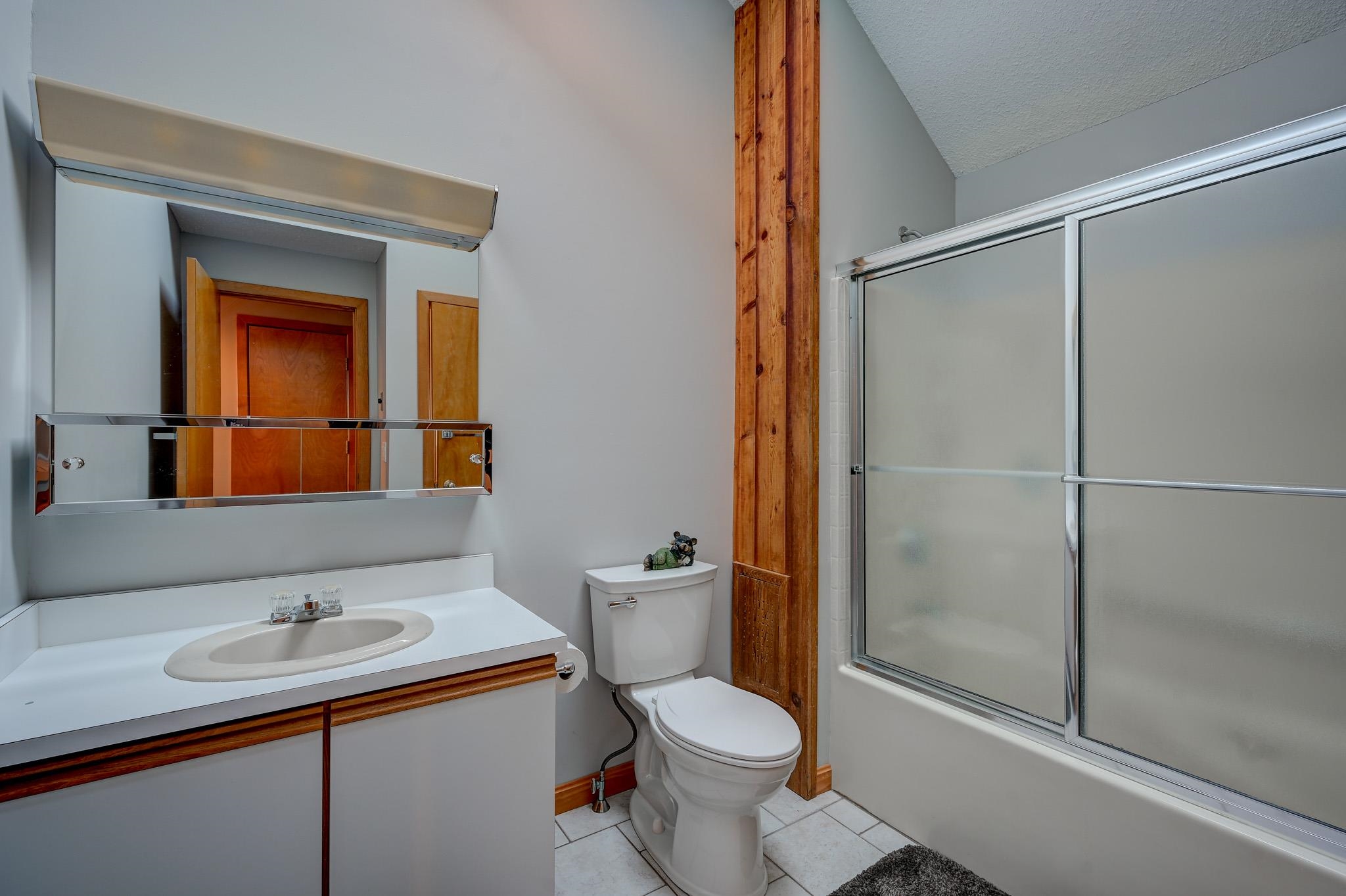 Bathroom with a white vanity, toilet, and frosted-glass sliding shower, accented by natural wood trim.