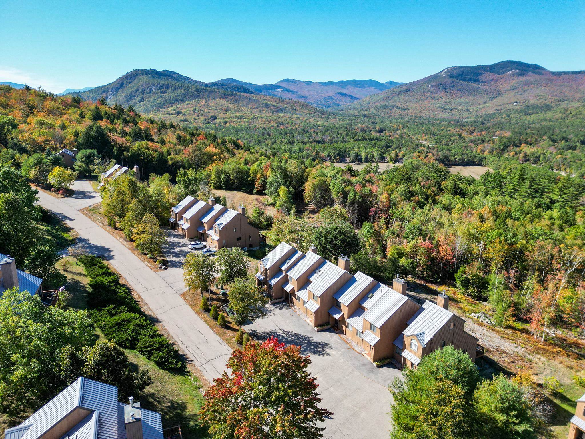 Aerial view of attached homes along a road, with autumn woods and mountains beyond.