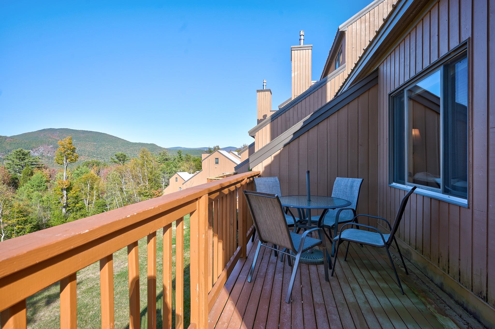 Furnished wooden balcony overlooking autumn trees and a forested mountain.