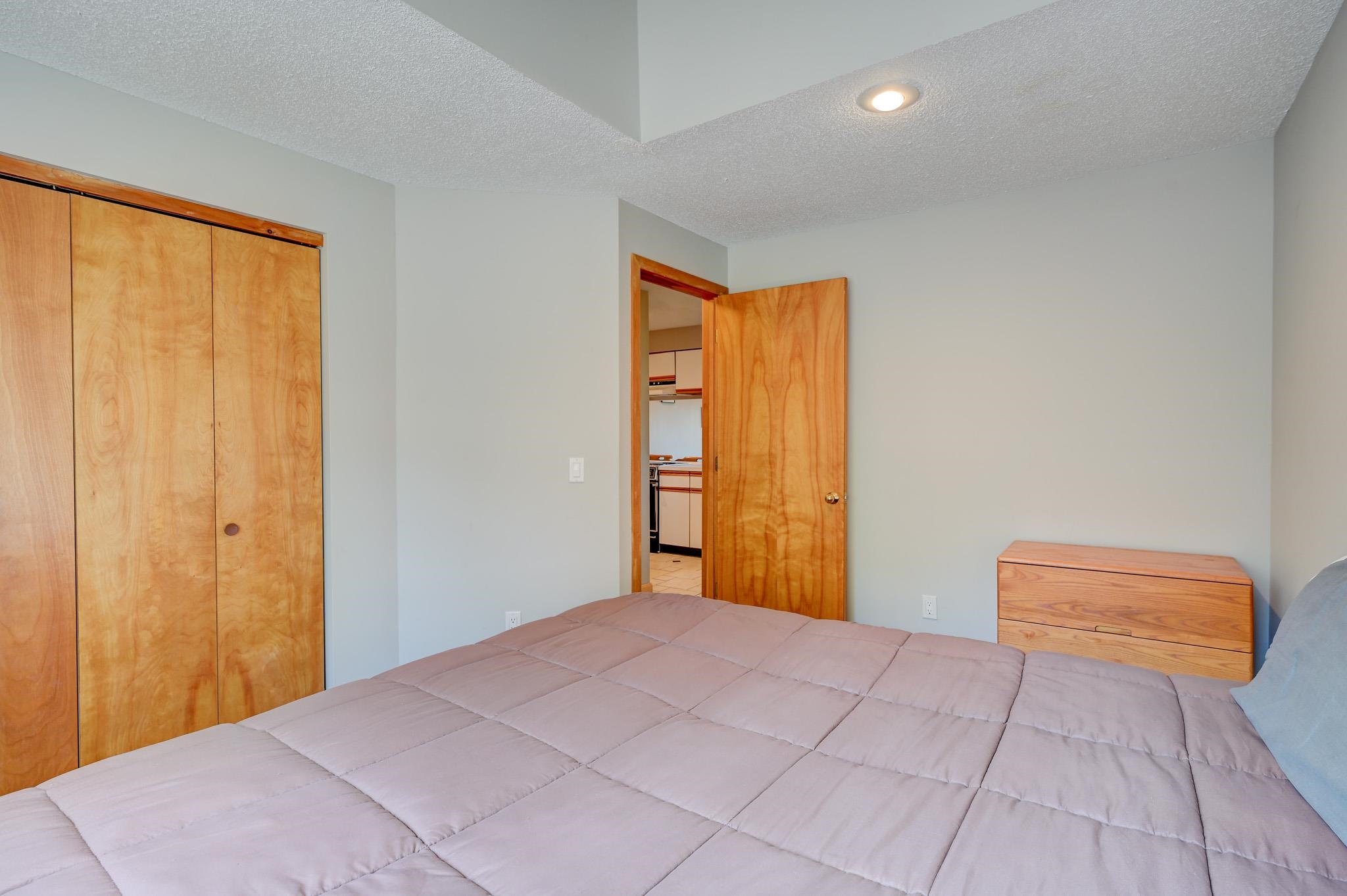 Bedroom with a large bed, wooden closet doors, and an open door to the kitchen.