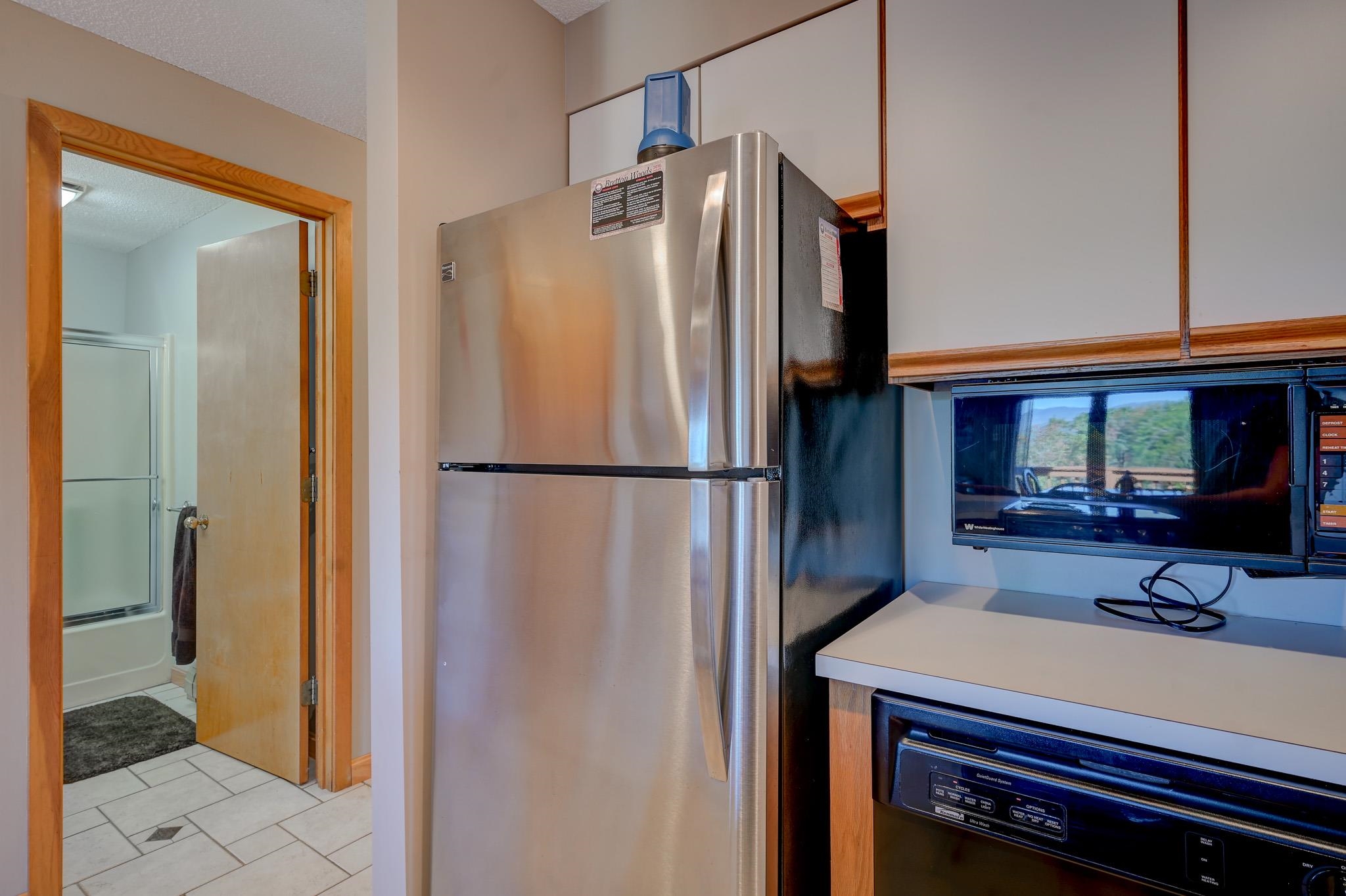 Kitchen with stainless steel refrigerator and built-in appliances beside an open bathroom doorway.