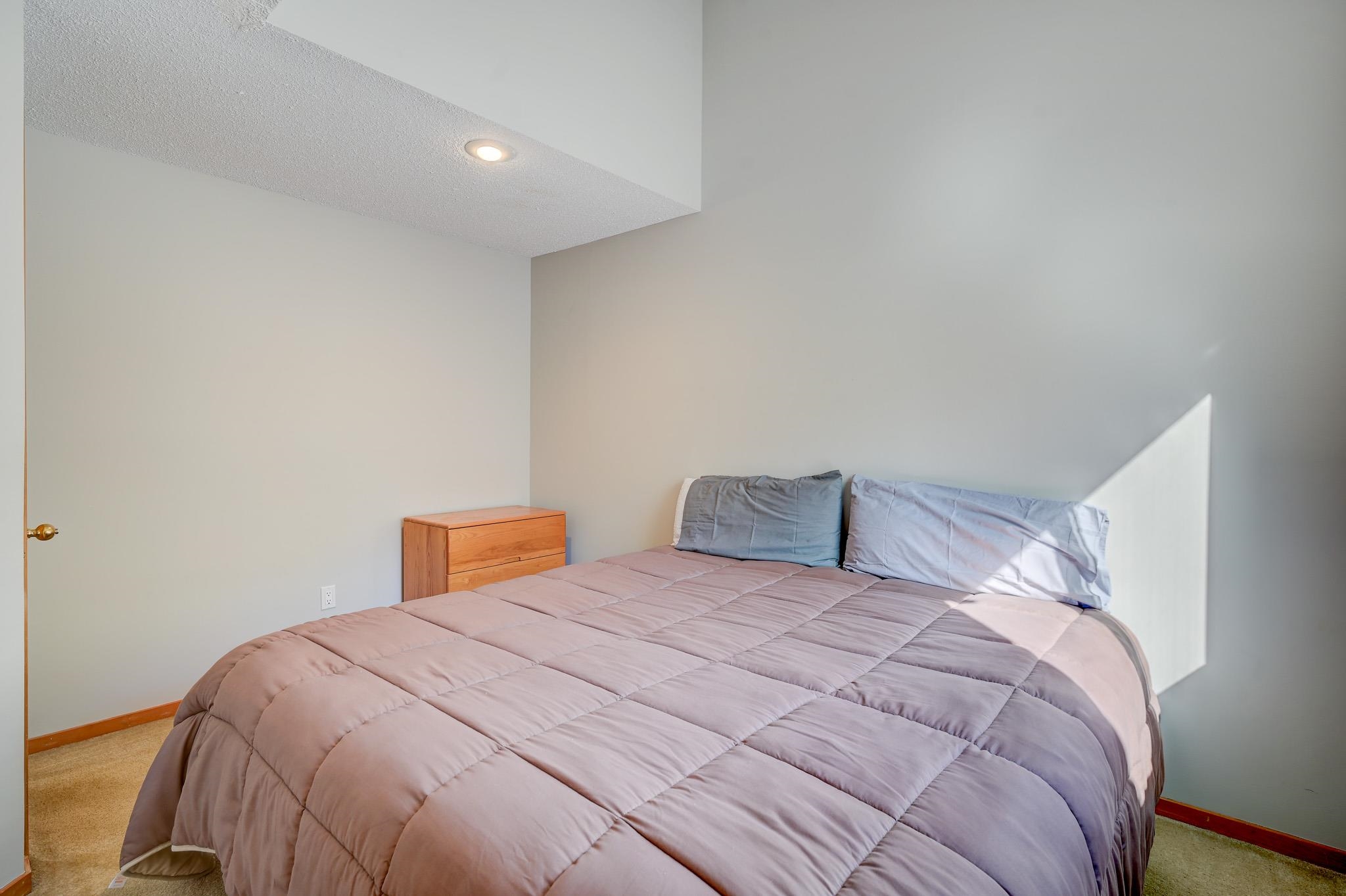 Bedroom with a mauve-gray quilted bed, blue-gray pillows, and sunlight across the wall.