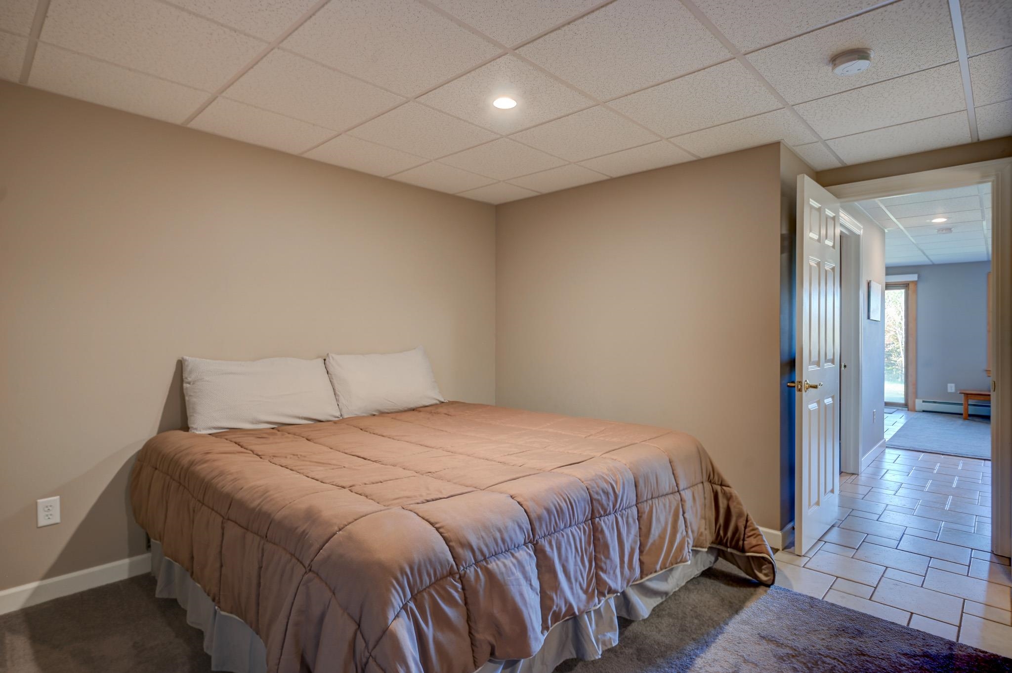 Bedroom with a tan-quilted bed and open doorway to a bright tiled room.