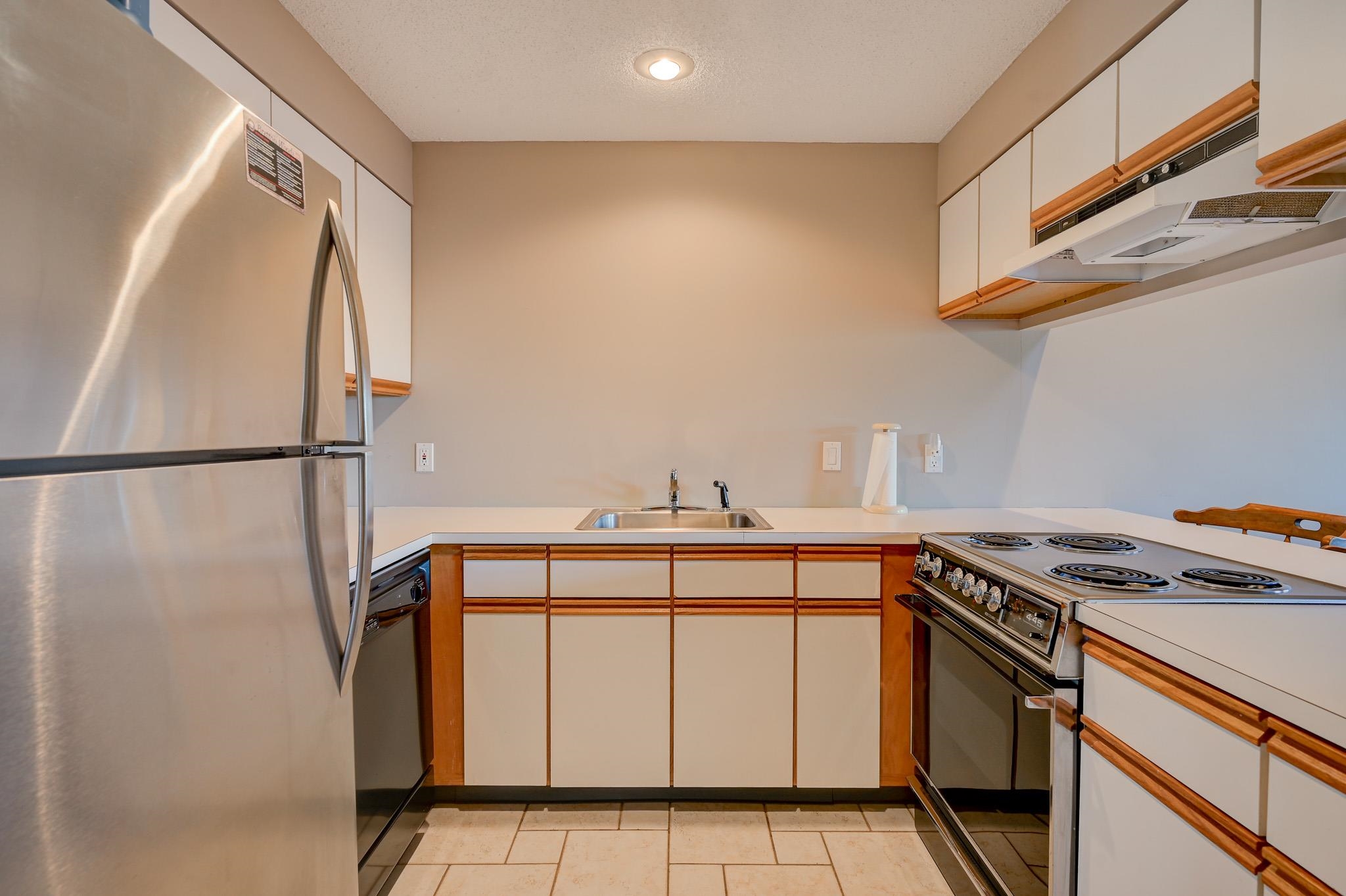 U-shaped kitchen with white wood-trimmed cabinets, stainless steel appliances, and a tiled floor.