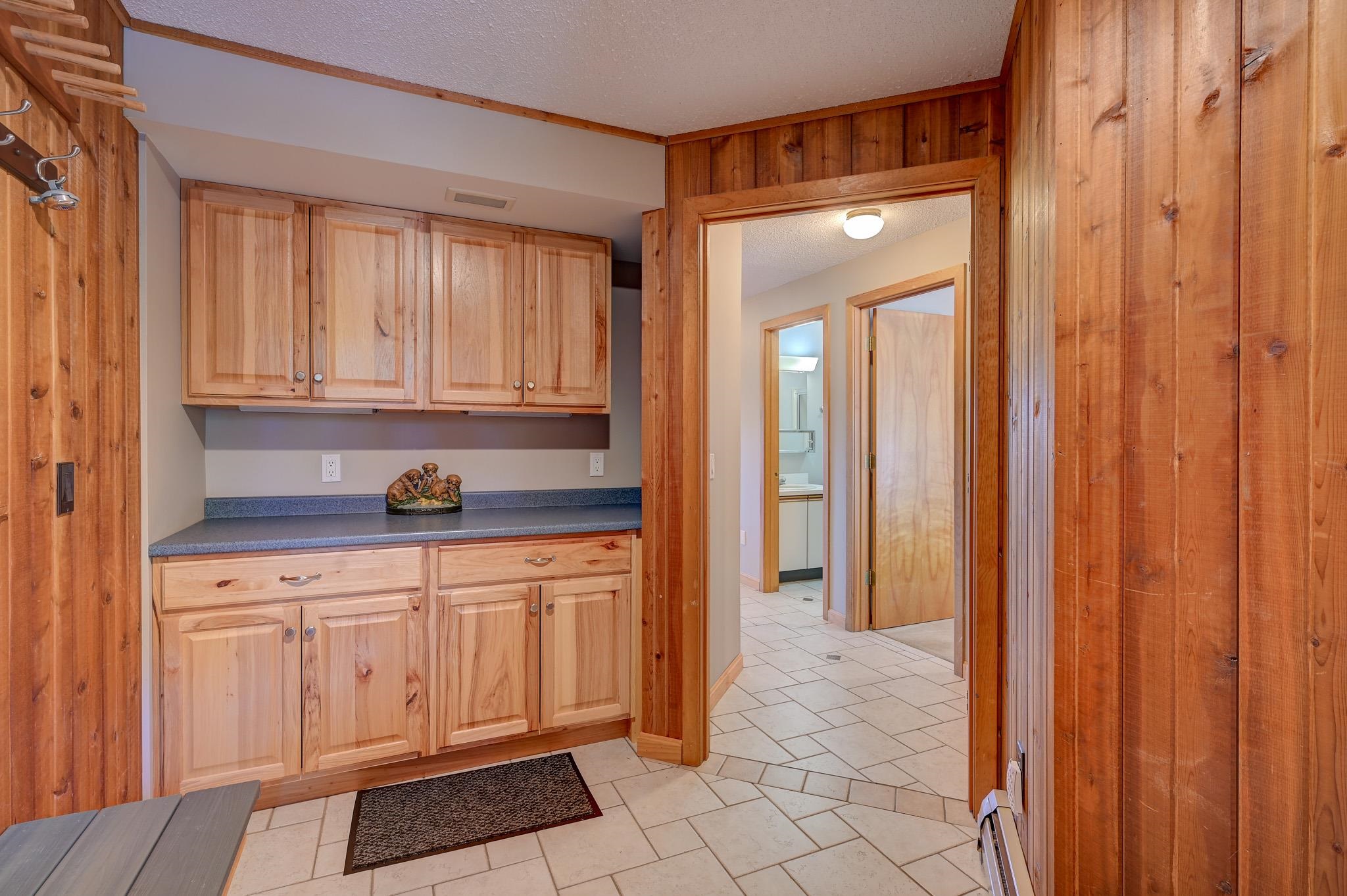 Wood-paneled mudroom with built-in cabinets, a blue countertop, wall hooks, and tiled flooring.