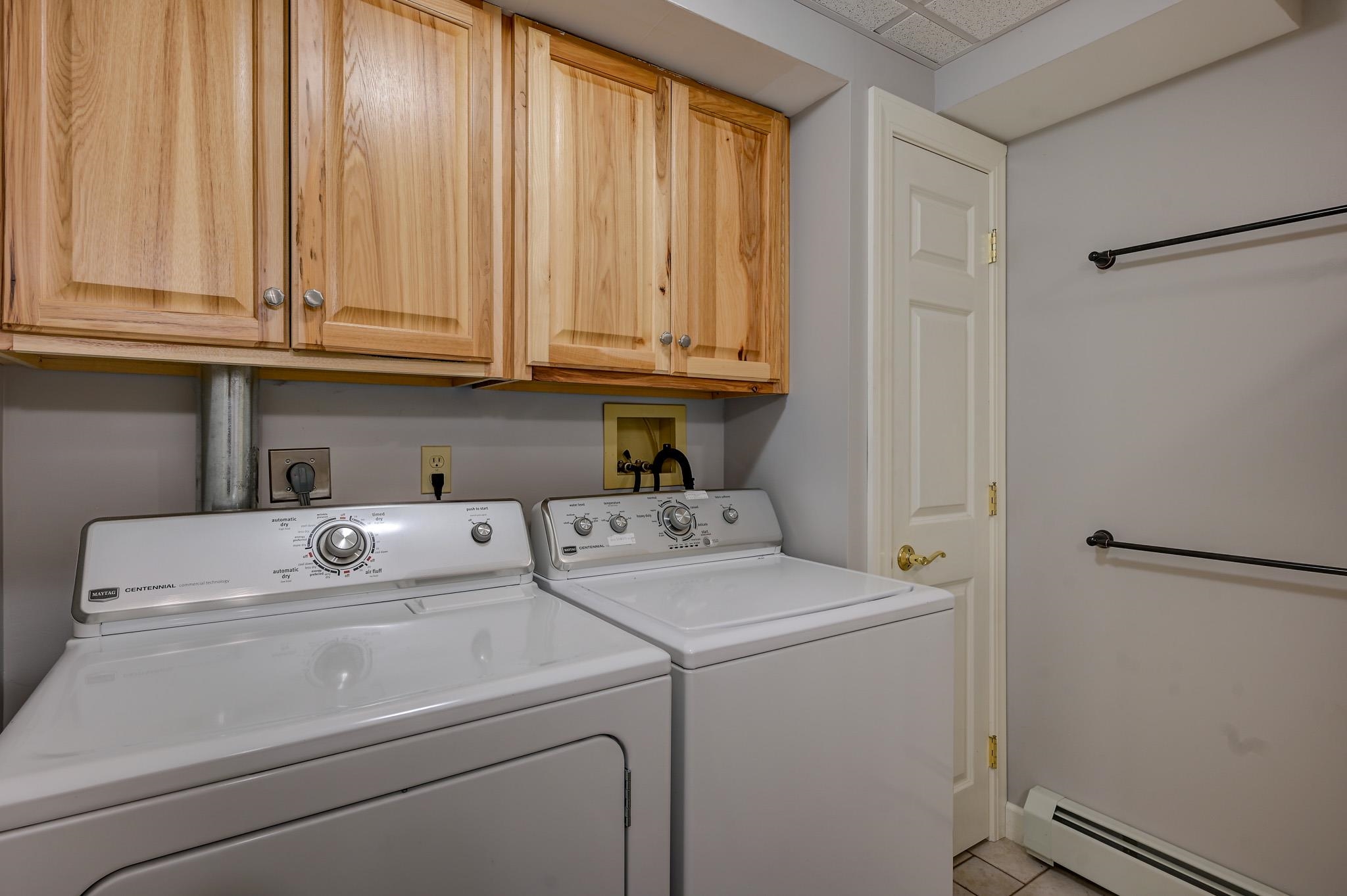 Laundry room with a white washer and dryer beneath natural wood cabinets.