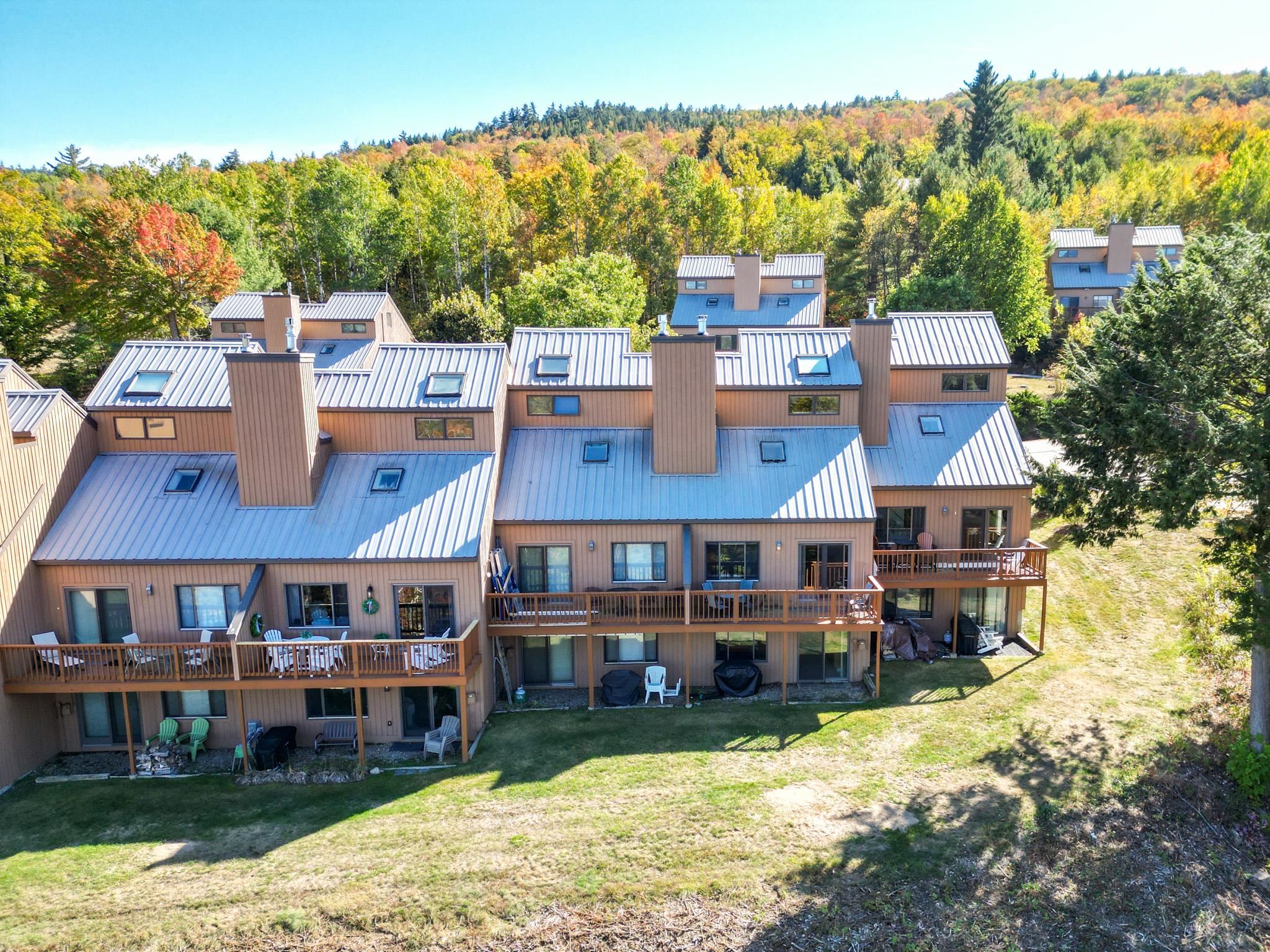 Aerial view of brown condominiums with long wooden decks below an autumn-colored wooded hillside.