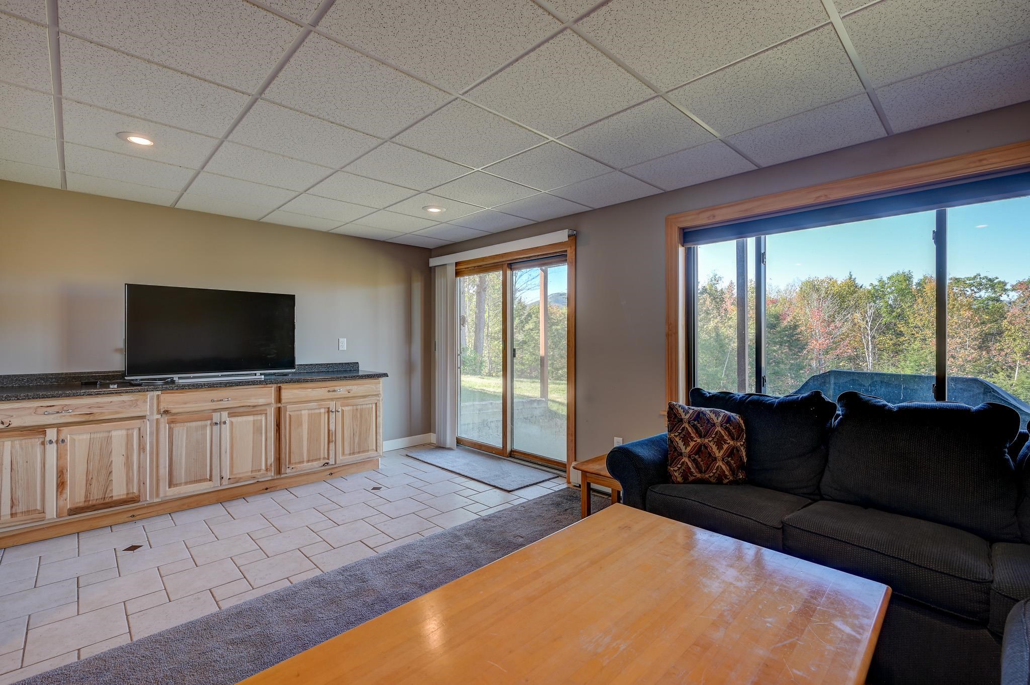 Living room with a wood media cabinet and sofa, opening to an autumn woodland view.