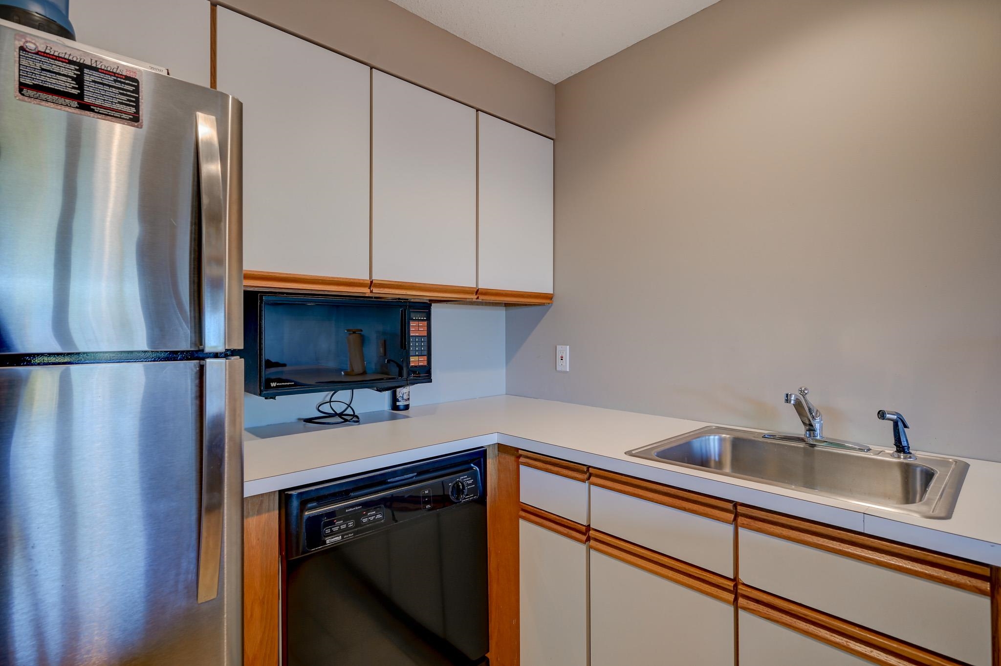 Compact kitchen with white and wood-trimmed cabinets, stainless refrigerator, and double-basin sink.