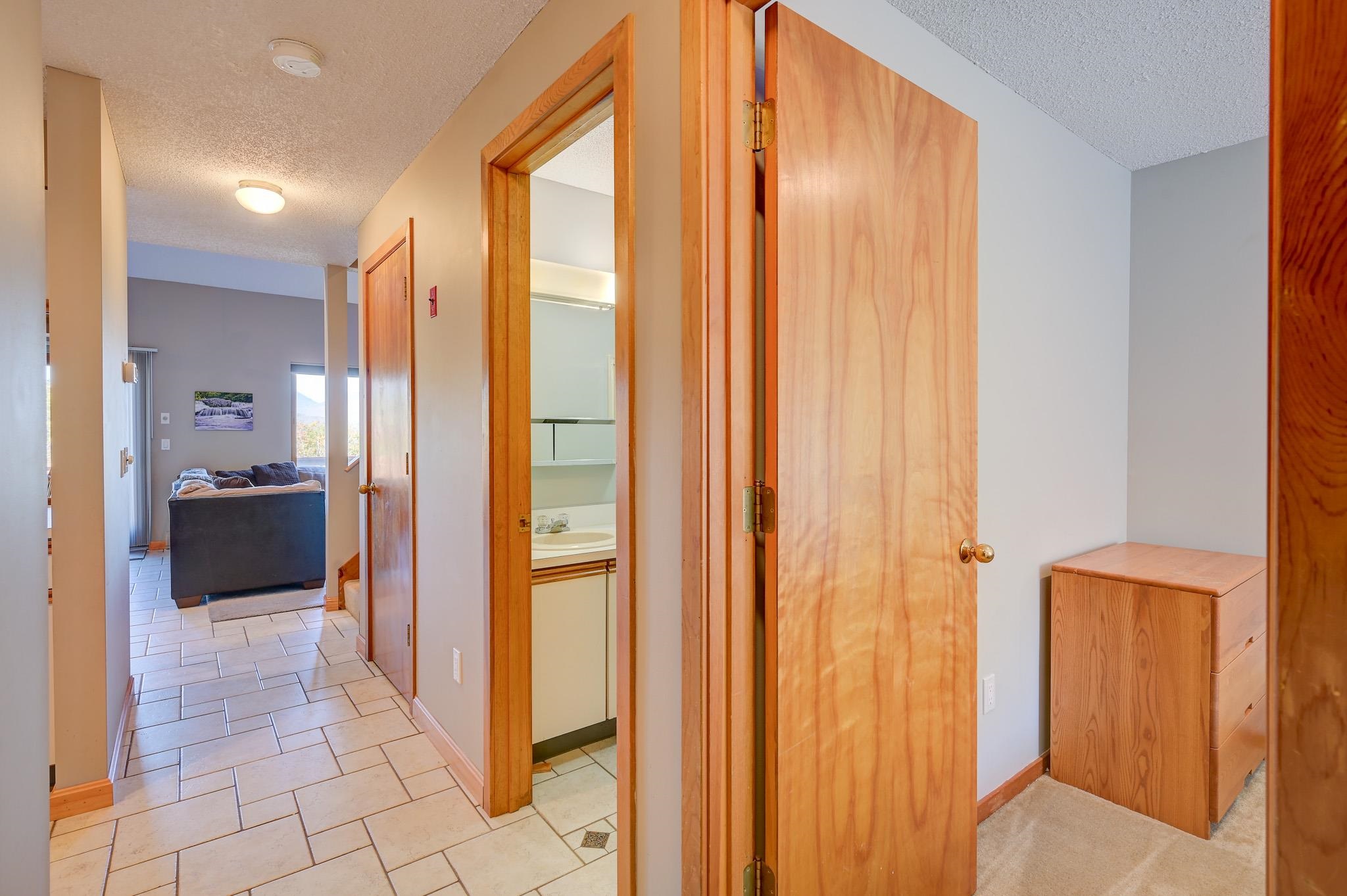 Tiled hallway with wood doors, a bathroom vanity, and a sofa visible in the adjoining living area.