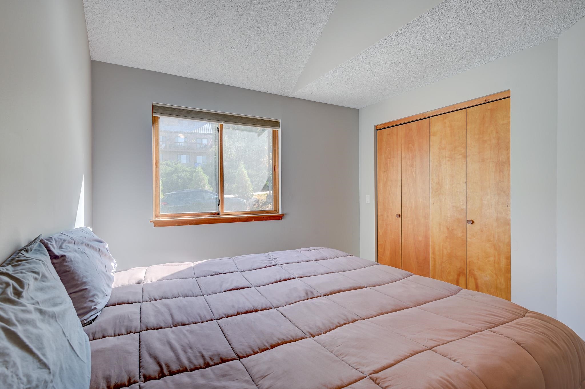 Bedroom with a large bed, wood-framed window, and built-in wooden closet doors.