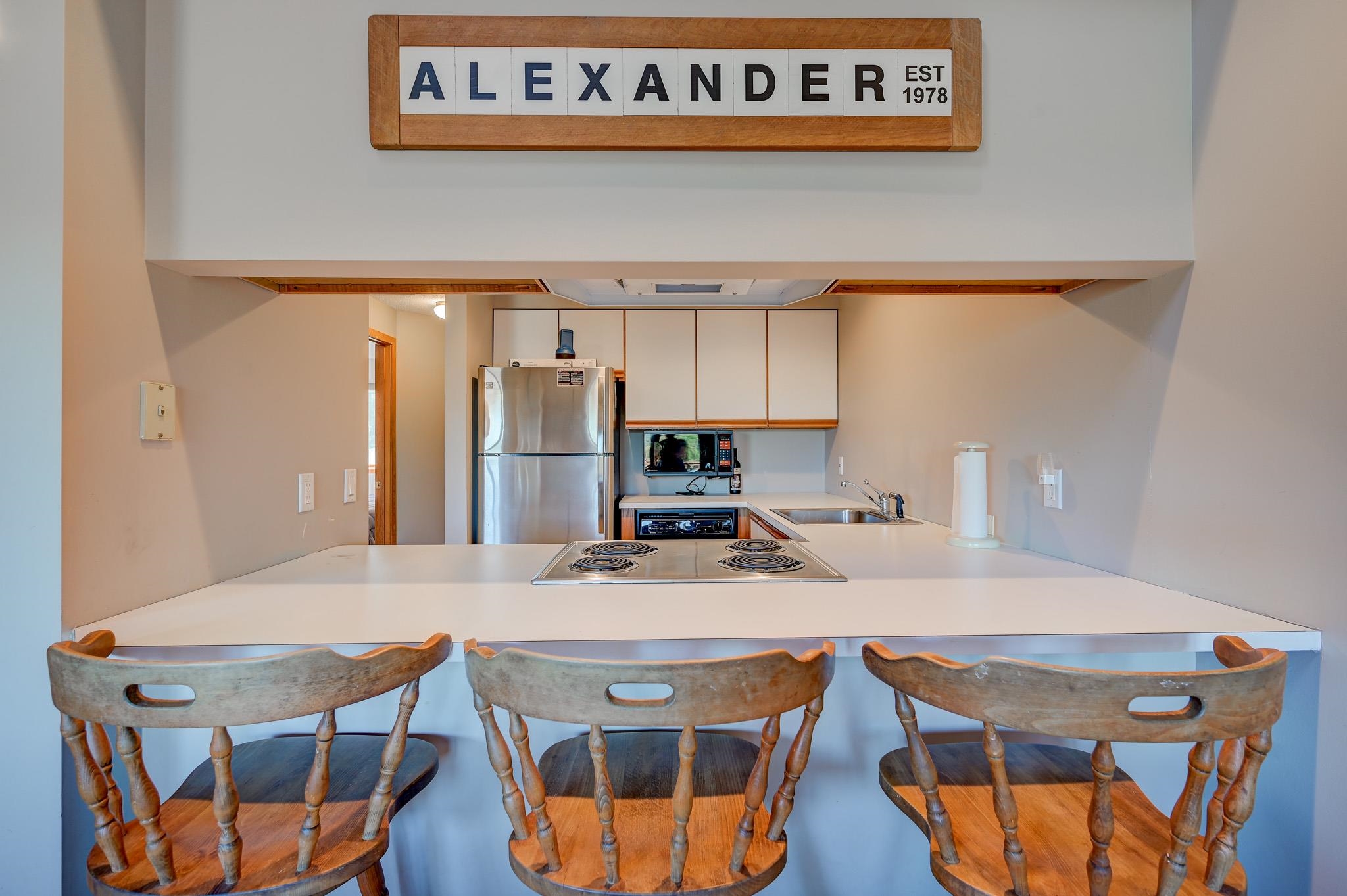 Kitchen with a white breakfast bar, three wooden stools, and a cooktop.