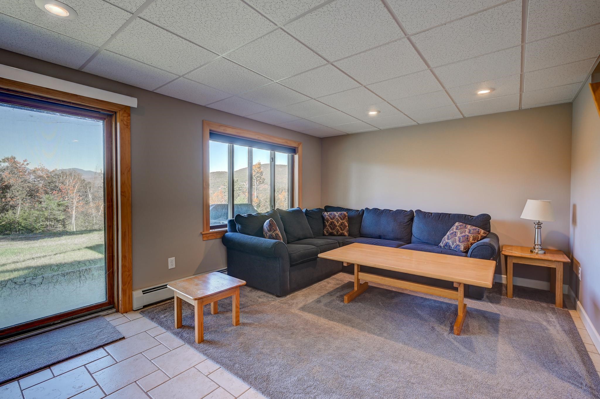 Living room with a dark blue sectional and large windows overlooking autumn trees and a mountain slope.