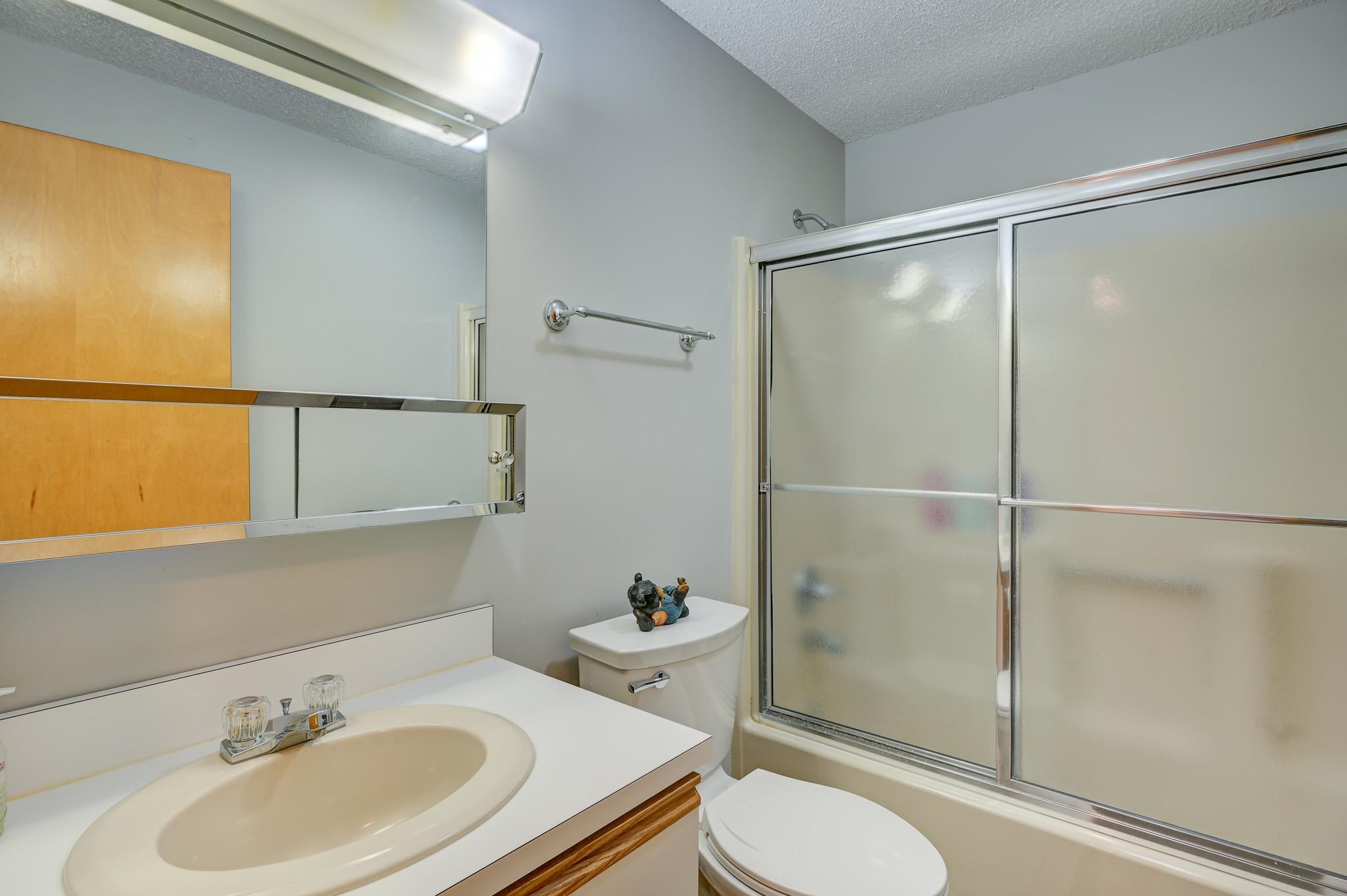 Bathroom with beige sink, mirrored cabinet, toilet, and tub with frosted sliding doors.