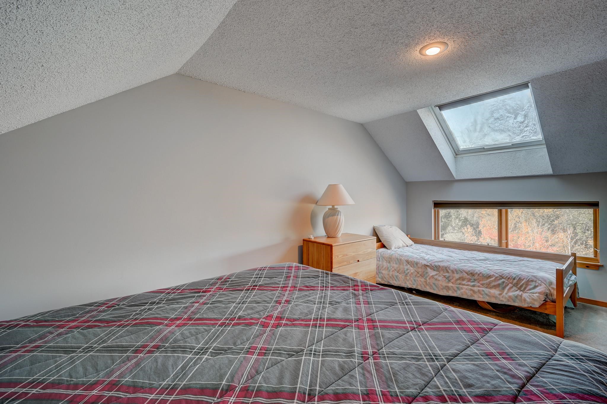 Attic bedroom with two beds, a skylight, and autumn trees visible through the windows.