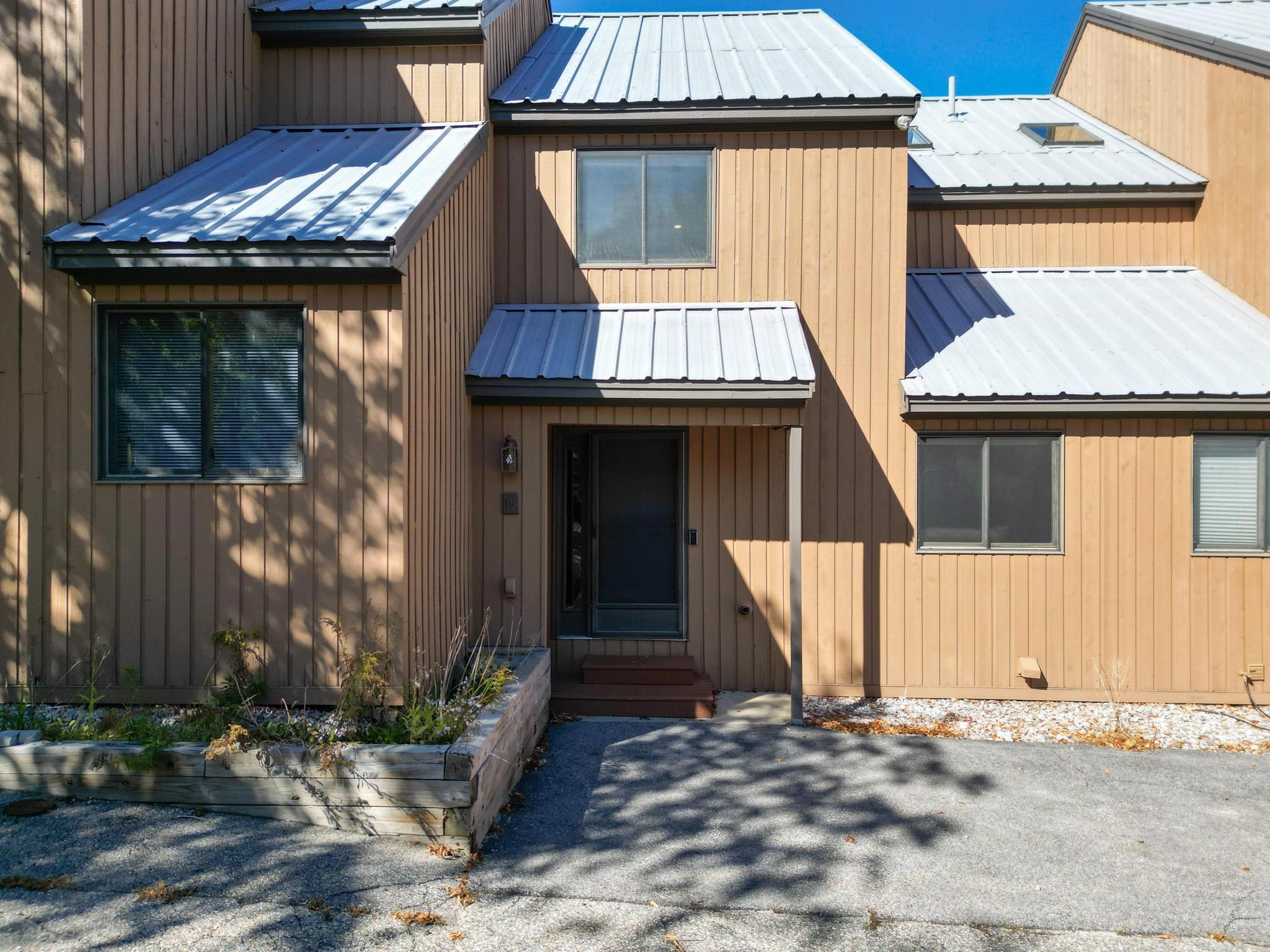 Brown multi-level home with silver metal roofs, a central entry, and a raised garden bed.