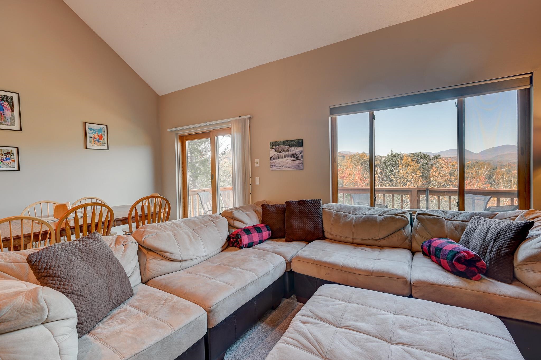 Living room with a beige sectional and wide windows overlooking autumn trees and distant mountains.