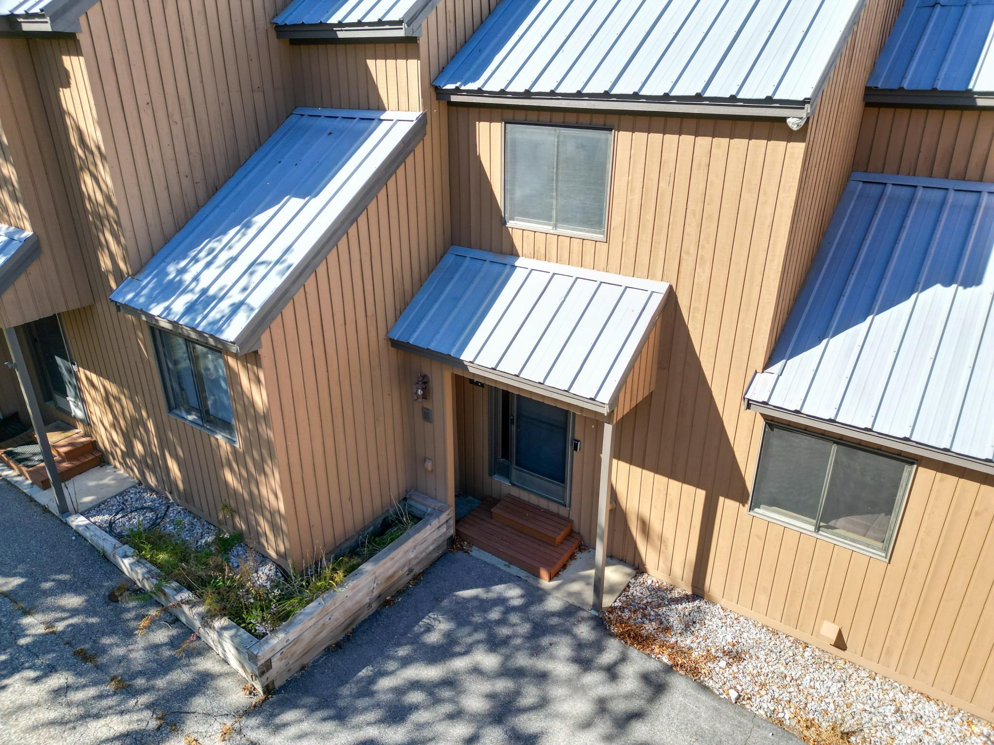 Brown-sided home with a metal roof, covered entry, and raised garden bed.