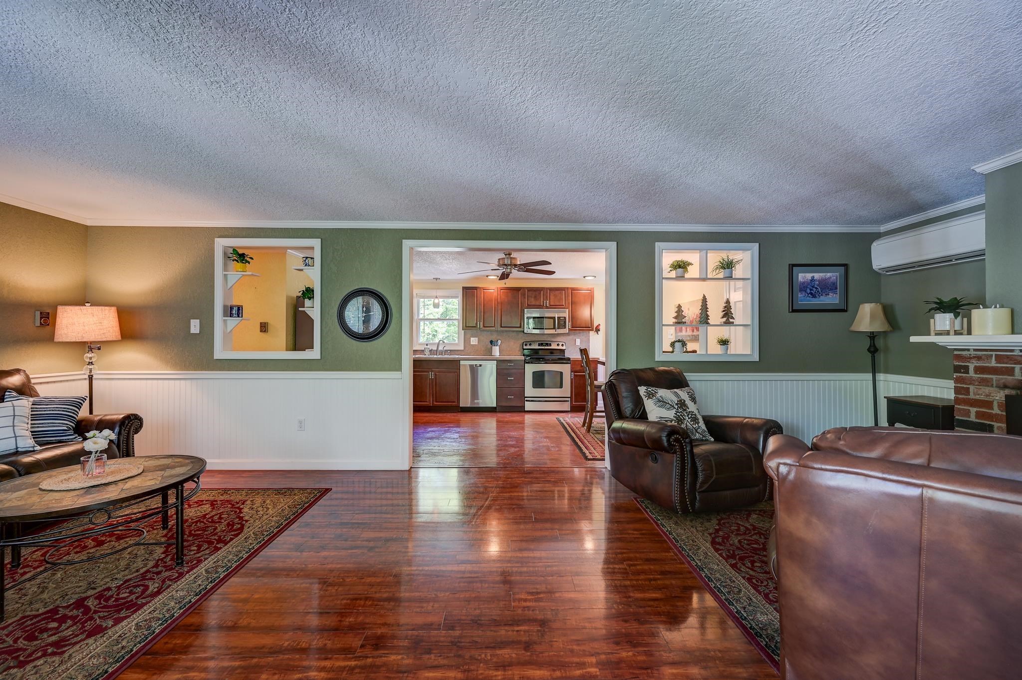 Living room with leather seating and polished wood floors, looking through to a kitchen with wood cabinets.