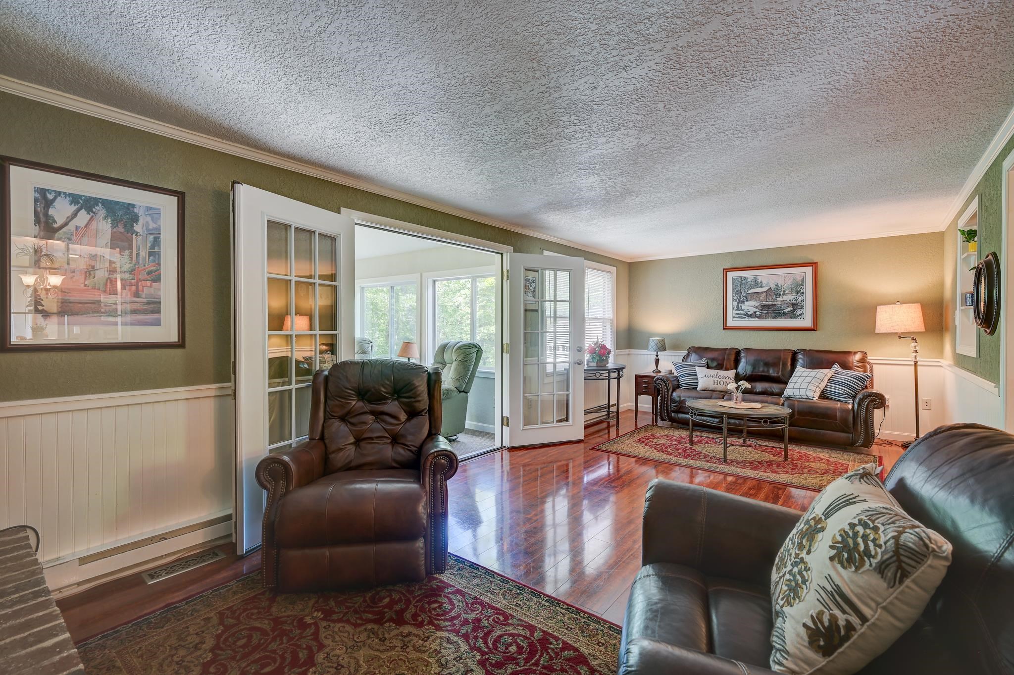 Furnished living room with leather seating, polished hardwood floors, and open French doors to a bright sunroom.