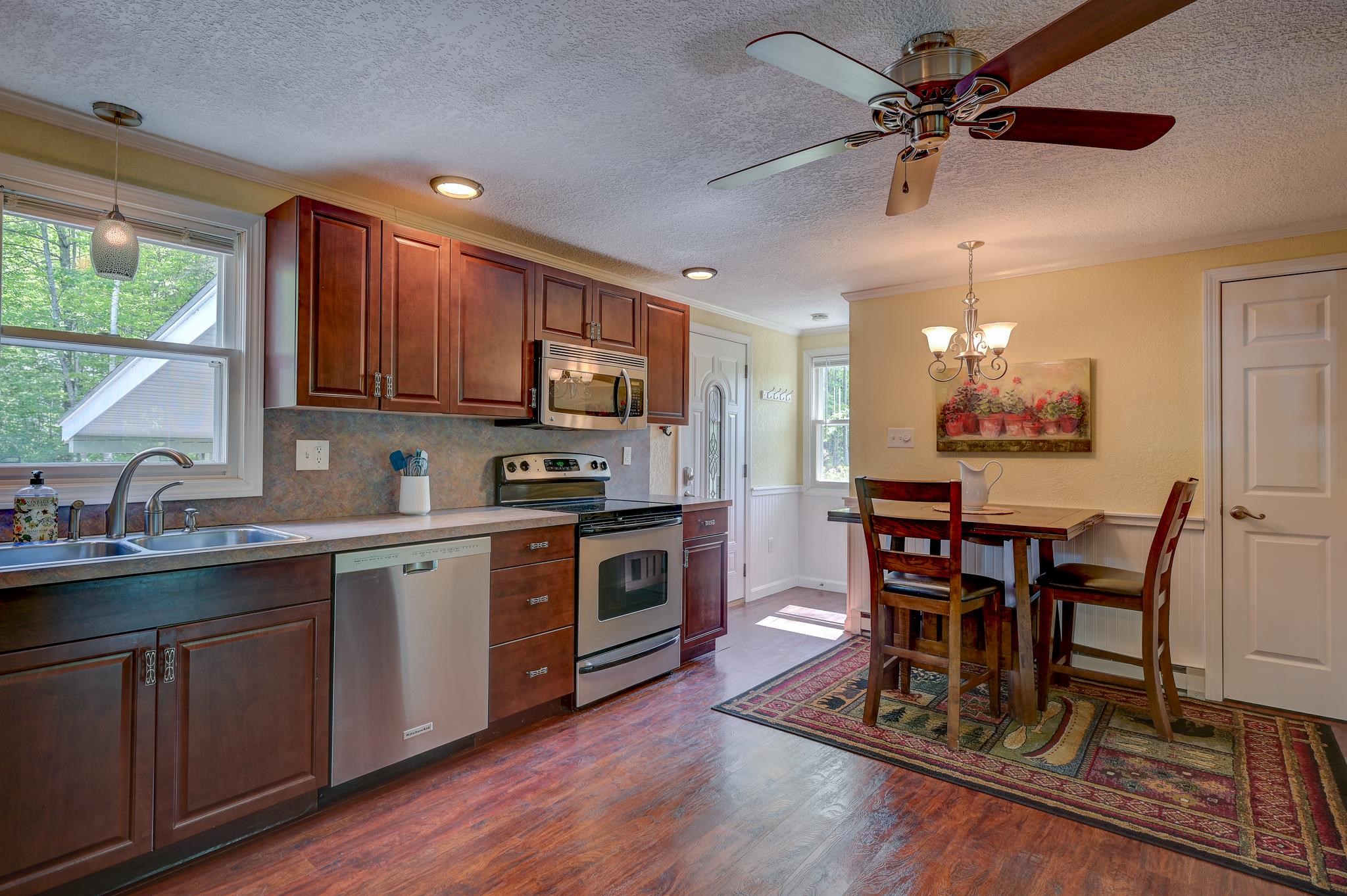 Kitchen and dining area with cherry cabinets, stainless steel appliances, and a wooden table on a patterned rug.