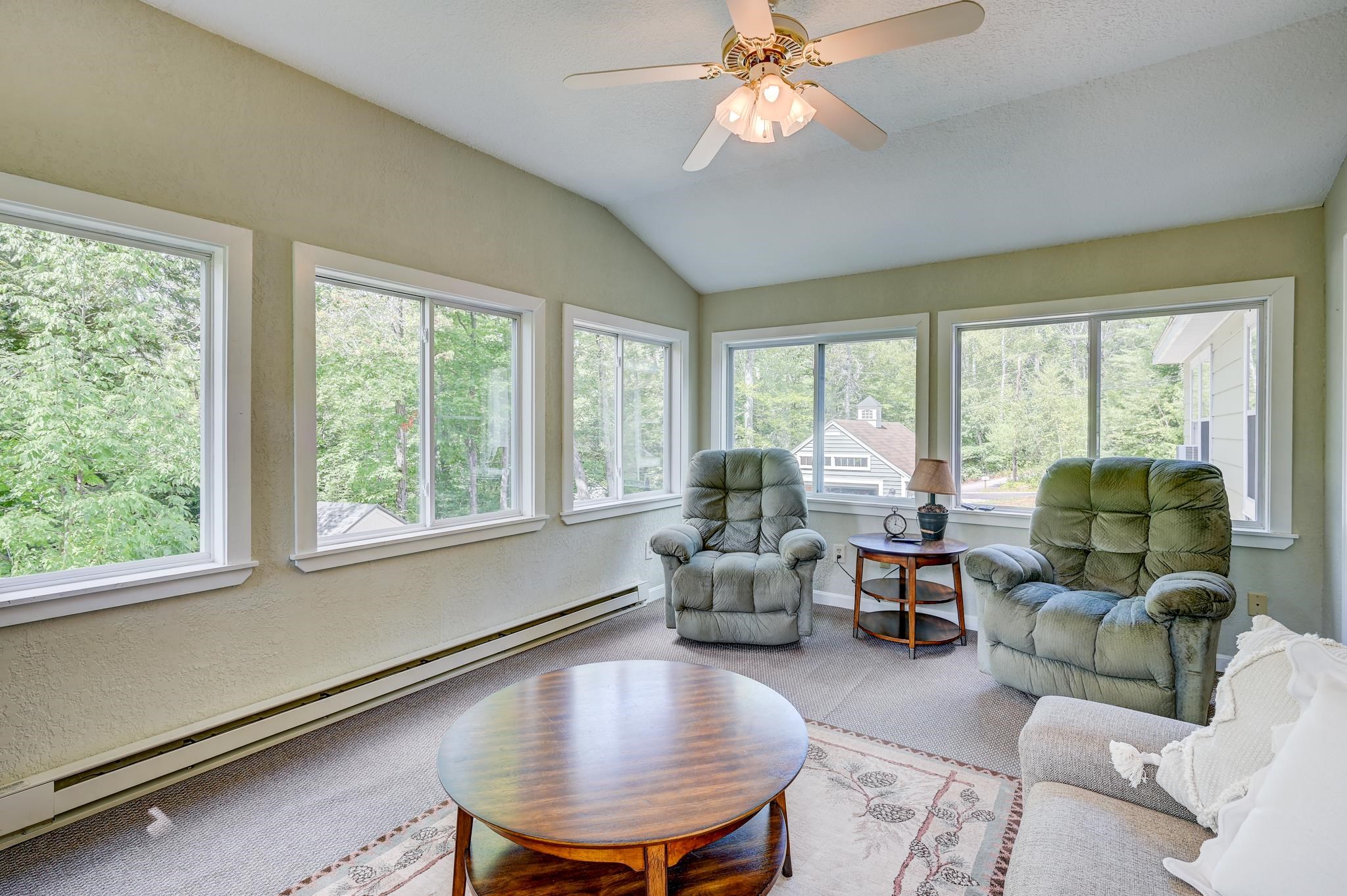 Living room with a vaulted ceiling, wide windows overlooking trees, two recliners, and a round coffee table.