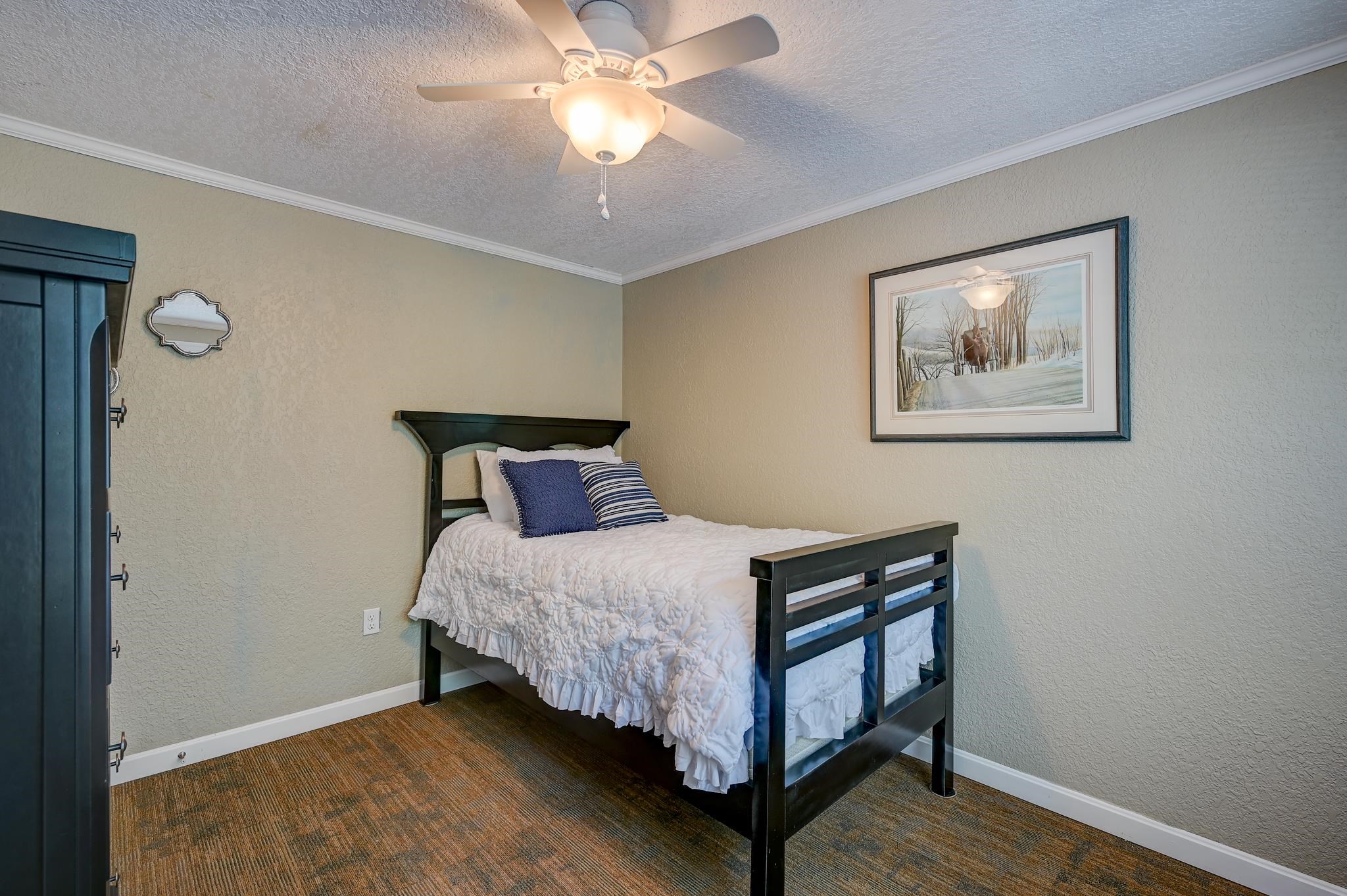 Furnished bedroom with a dark wood bed, white quilt, and ceiling fan with a lit fixture.