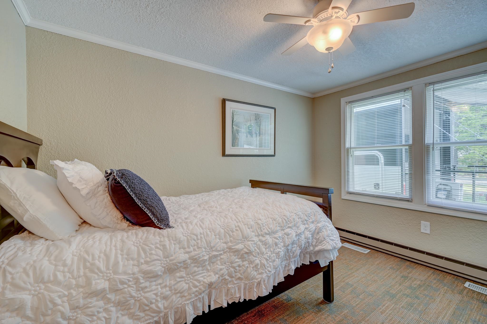 Bedroom with a white quilted bed, two bright windows, and a ceiling fan.