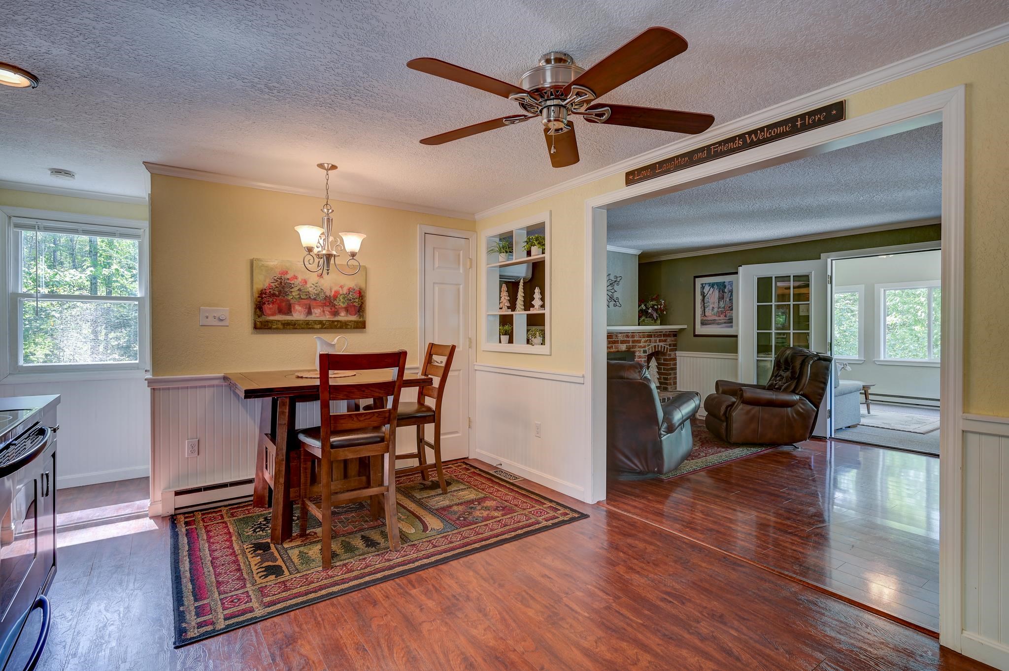 Dining area with a wooden table and patterned rug, opening into a living room with leather recliners.