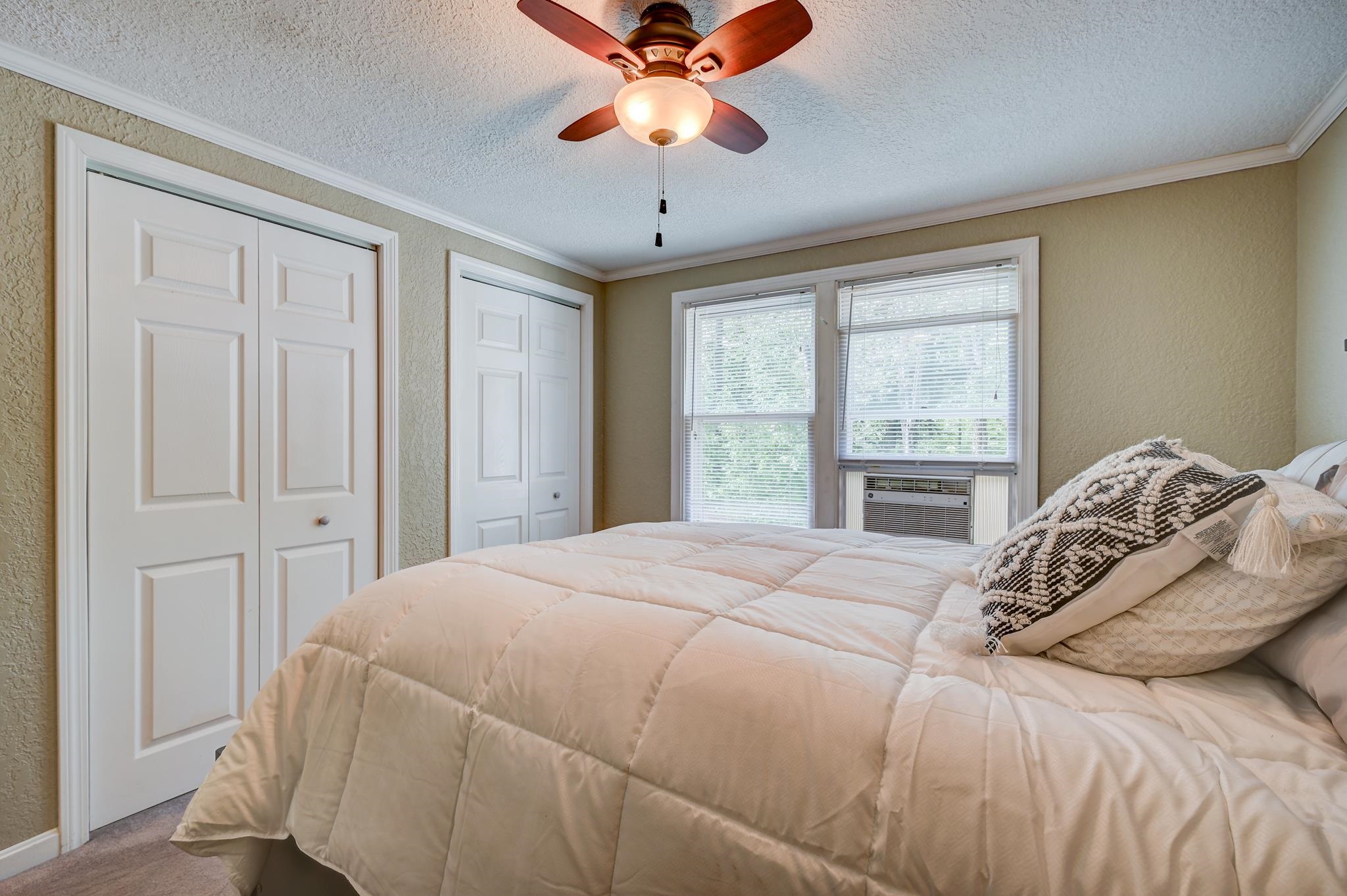 Bedroom with a pale quilted bed, double closet doors, window air conditioner, and ceiling fan.