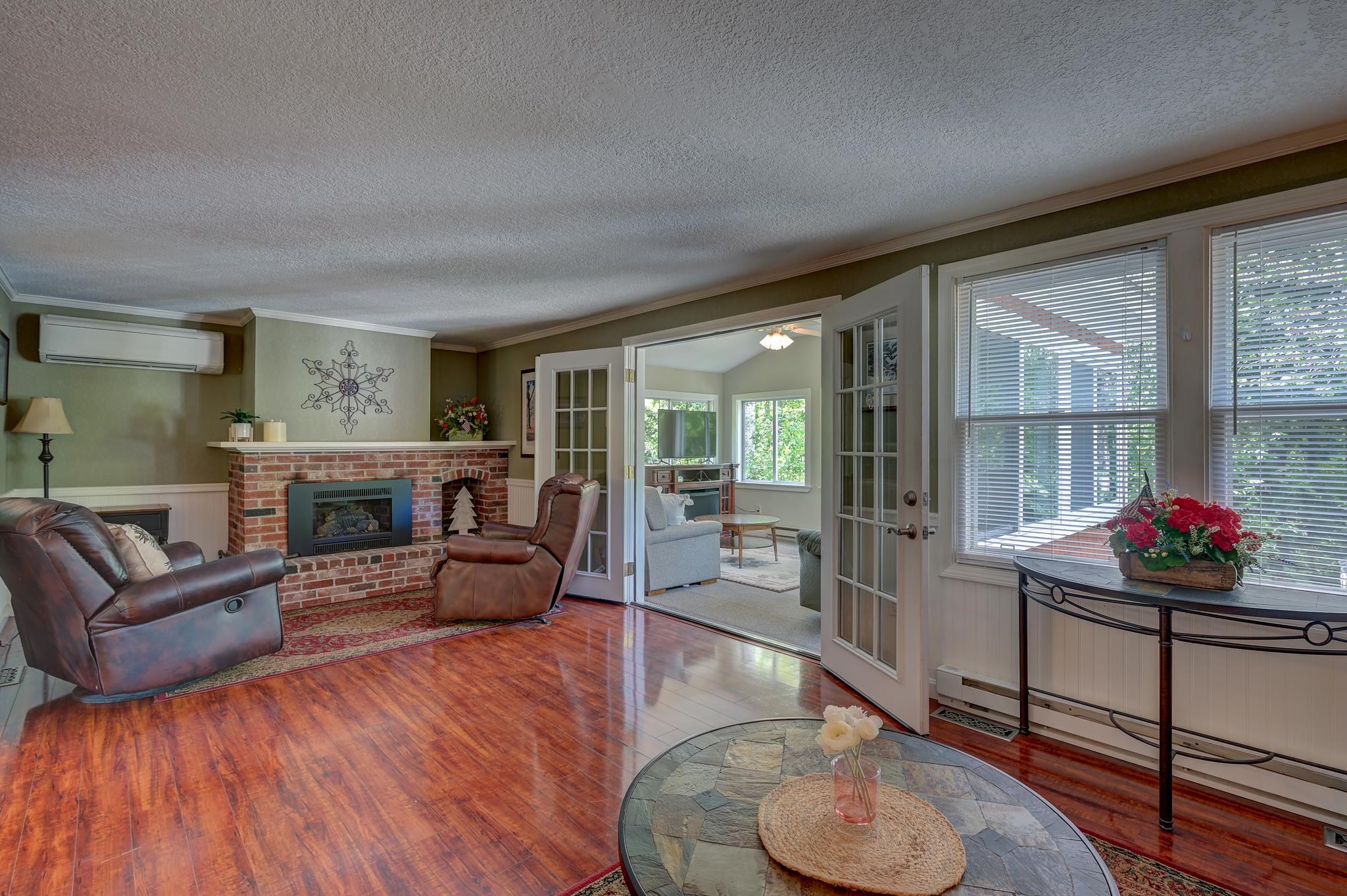 Living room with a brick fireplace, leather recliners, and glass doors to a bright adjoining sitting room.