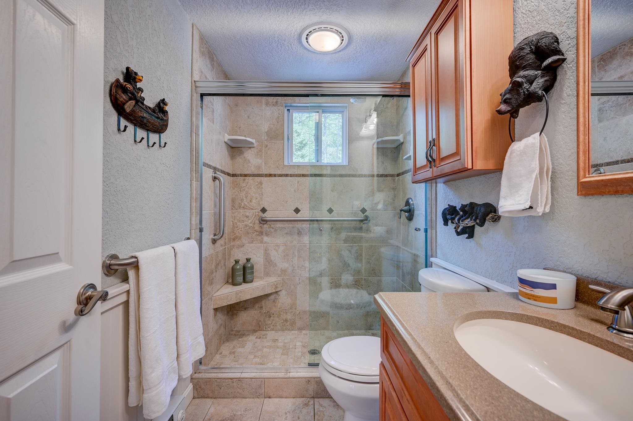 Bathroom with a glass-enclosed tiled shower, built-in bench, and wood vanity.
