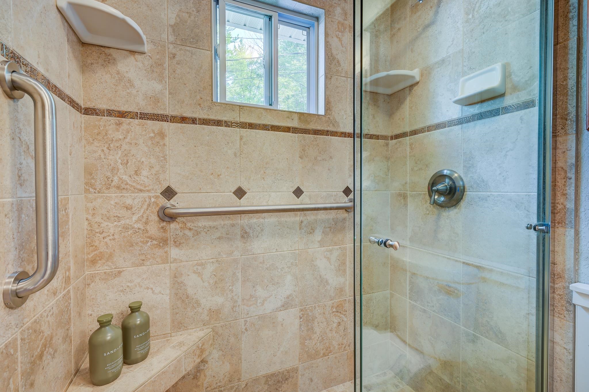 Walk-in shower with beige tile, glass enclosure, grab bars, and a built-in bench.