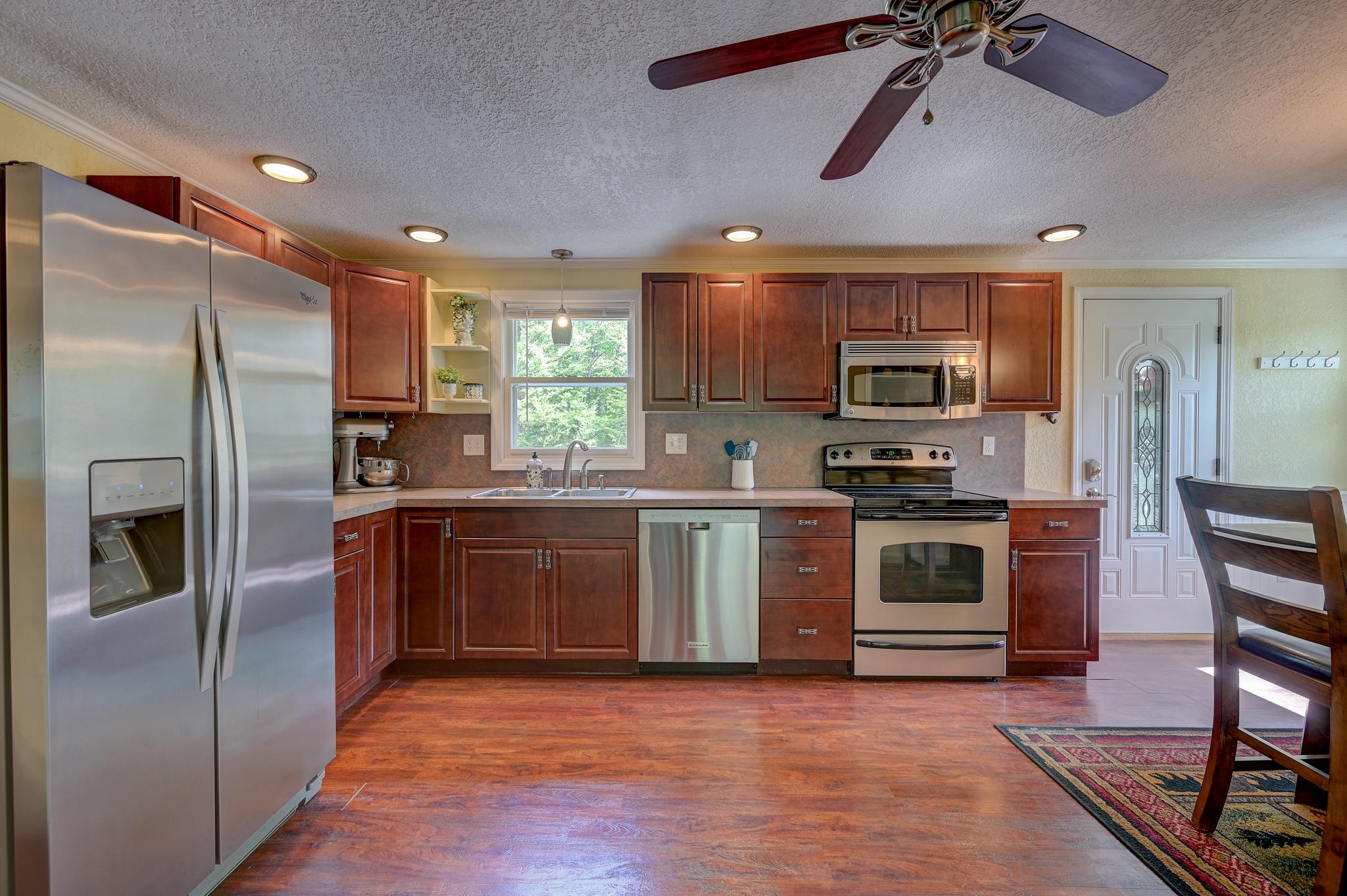 Kitchen with reddish-brown cabinets, stainless steel appliances, and a window above the sink.
