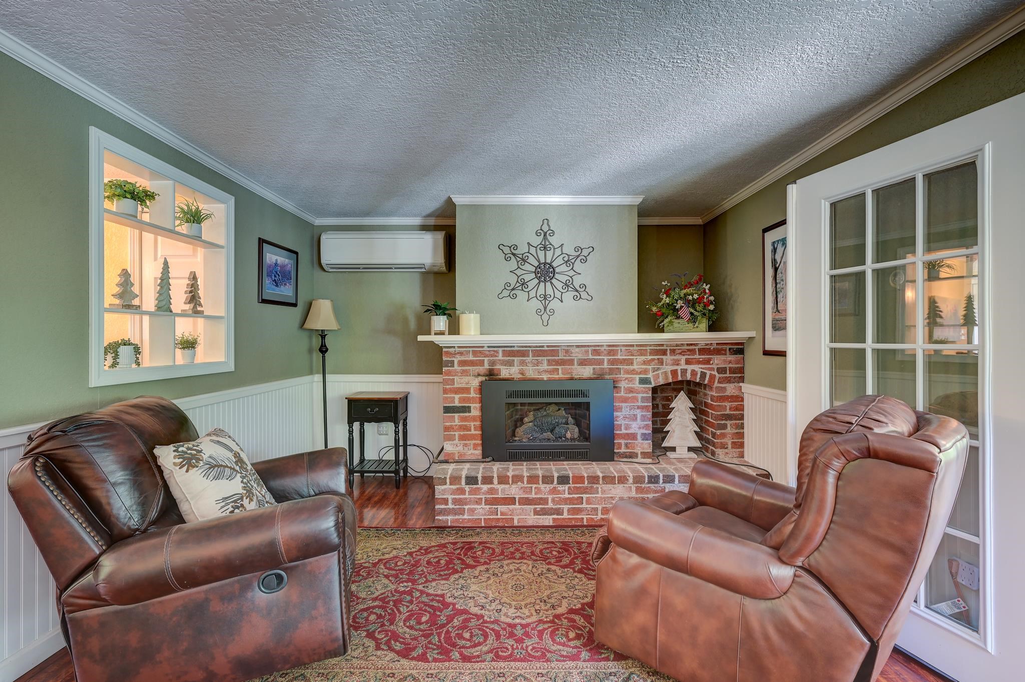 Living room with brown leather recliners, a brick fireplace, and a red patterned rug.
