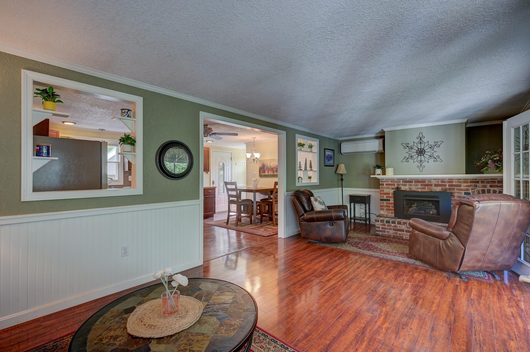 Living room with brick fireplace, brown leather recliners, and reddish hardwood floors.
