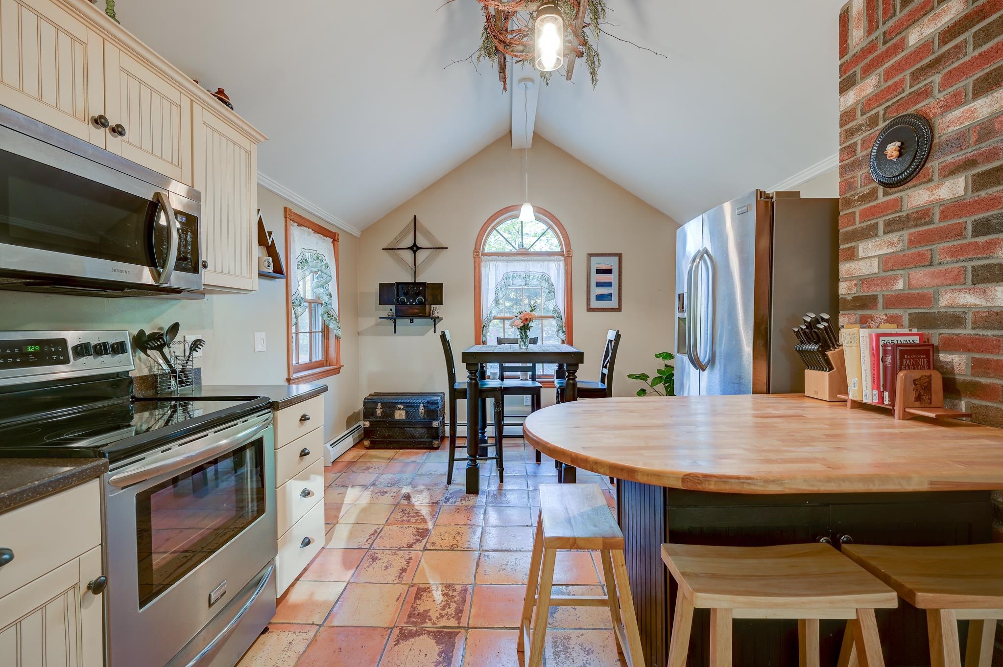Kitchen with a large rounded wood island, terracotta tile floor, and dining nook beneath an arched window.