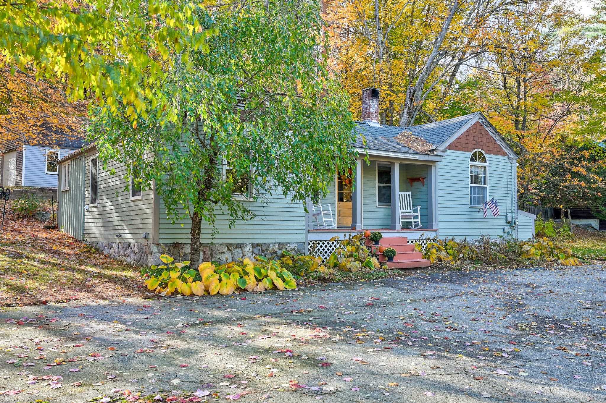 Blue-sided house with a covered porch and arched window amid autumn foliage.