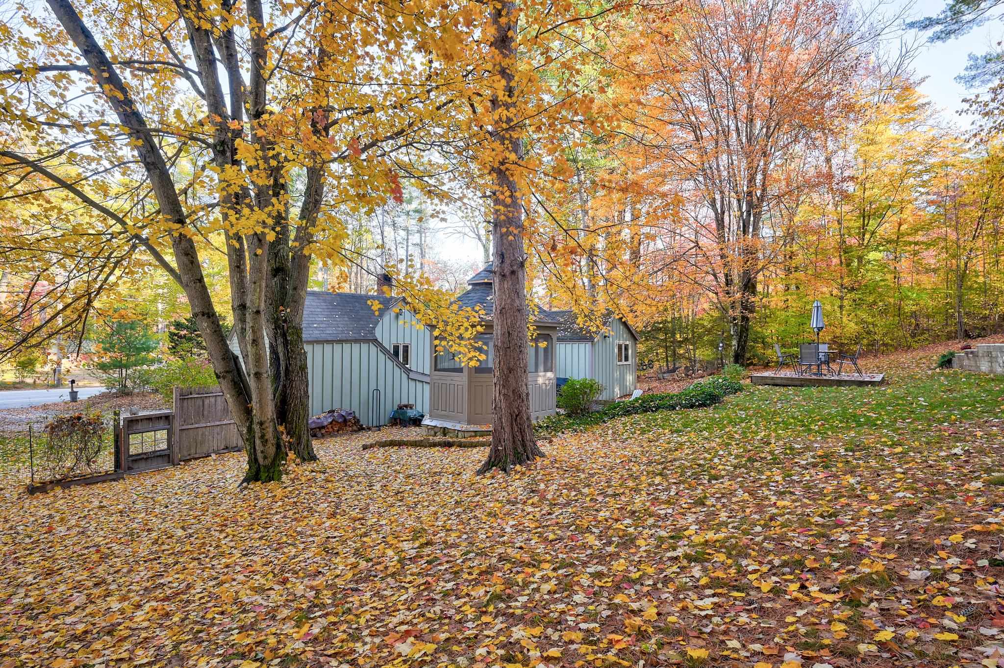 House nestled among autumn trees beside a leaf-covered yard and patio seating.