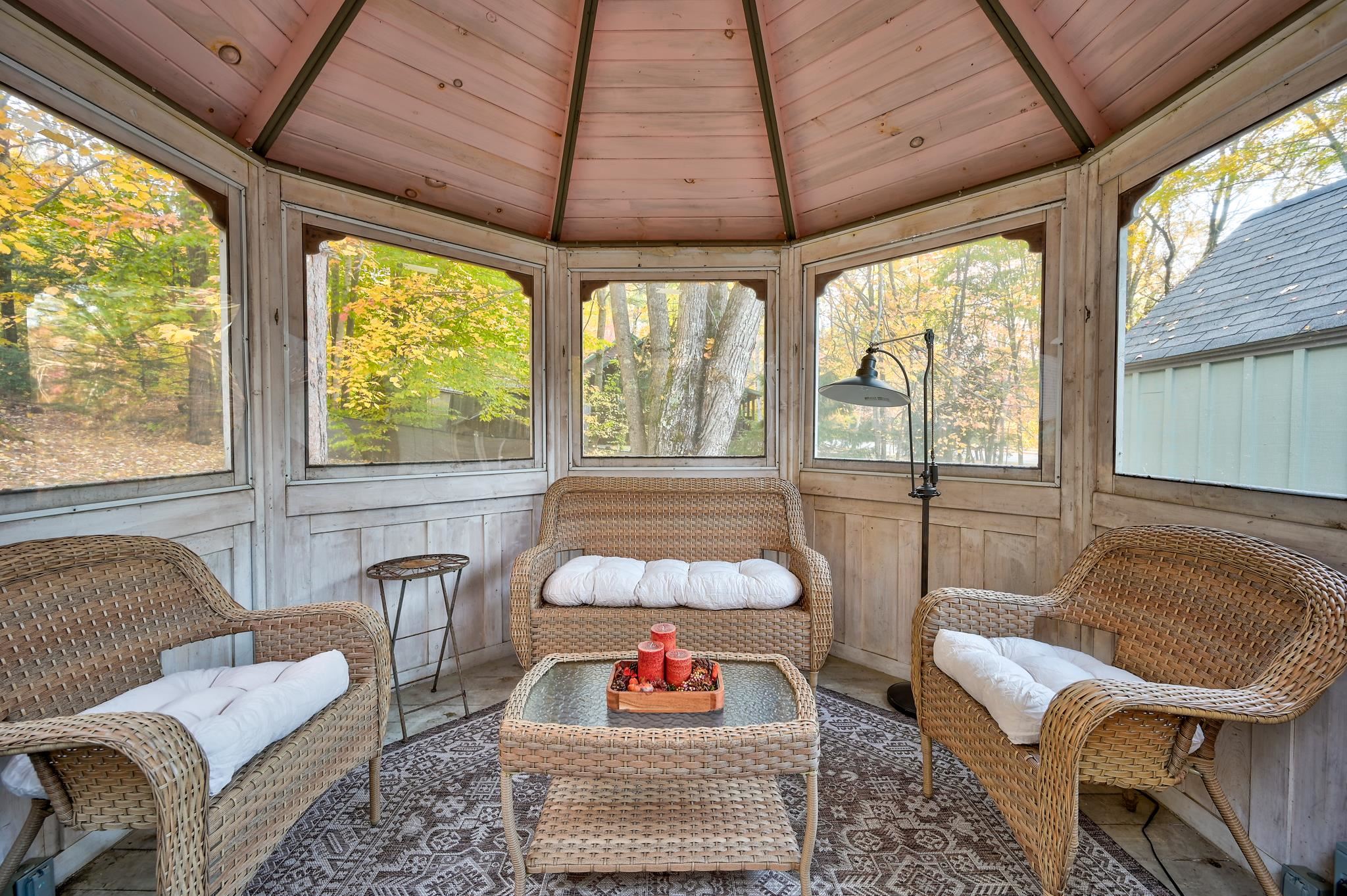 Enclosed sunroom with wicker chairs and a loveseat, overlooking autumn trees.