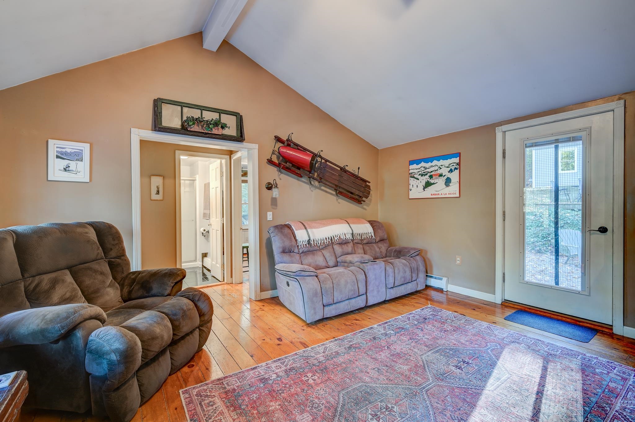 Furnished living room with a sloped ceiling, reclining sofas, wood floors, and a vintage sled on the wall.