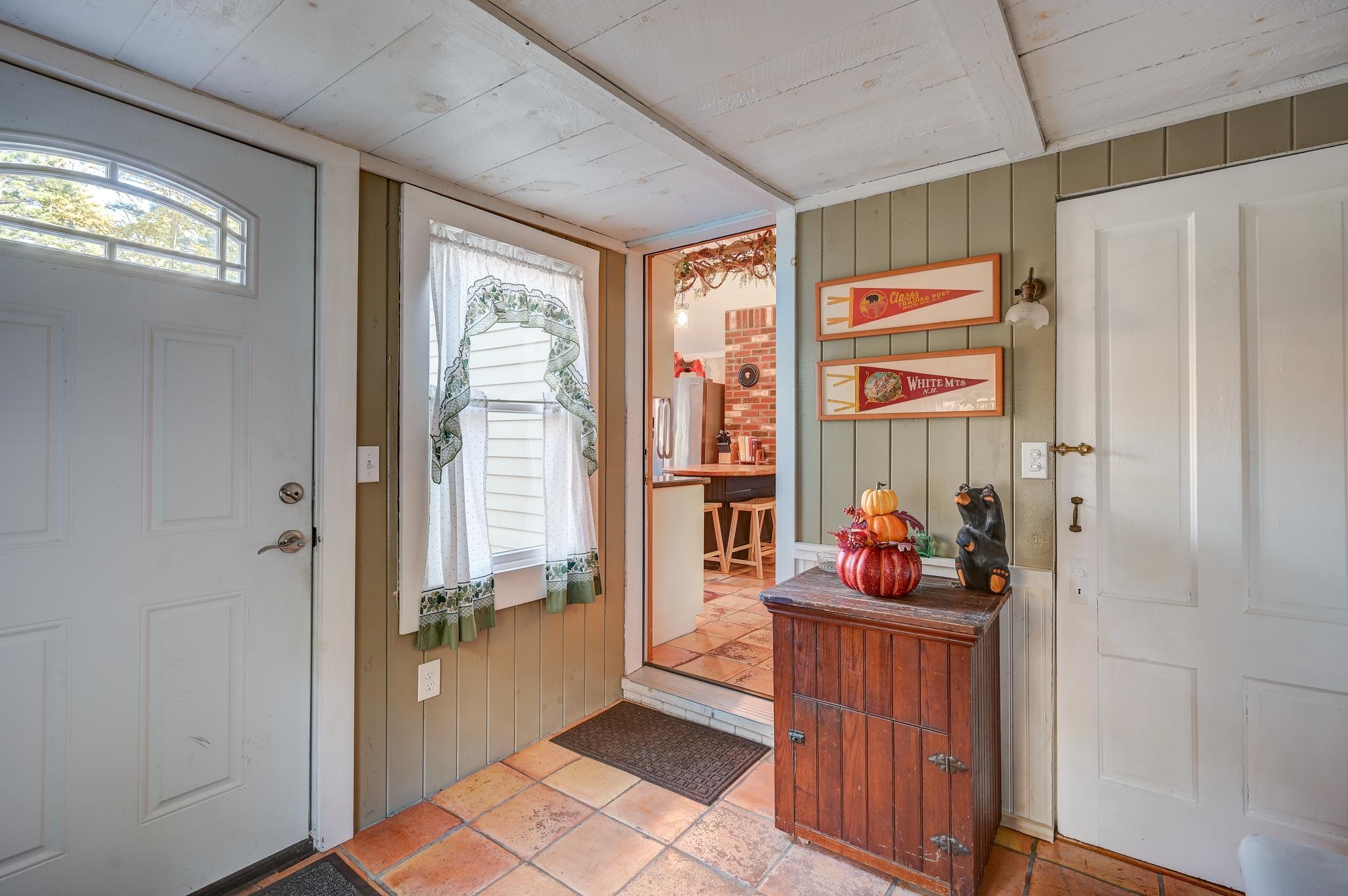 Entry foyer with terracotta tile floors, a curtained window, and a wooden cabinet topped with pumpkin decor.