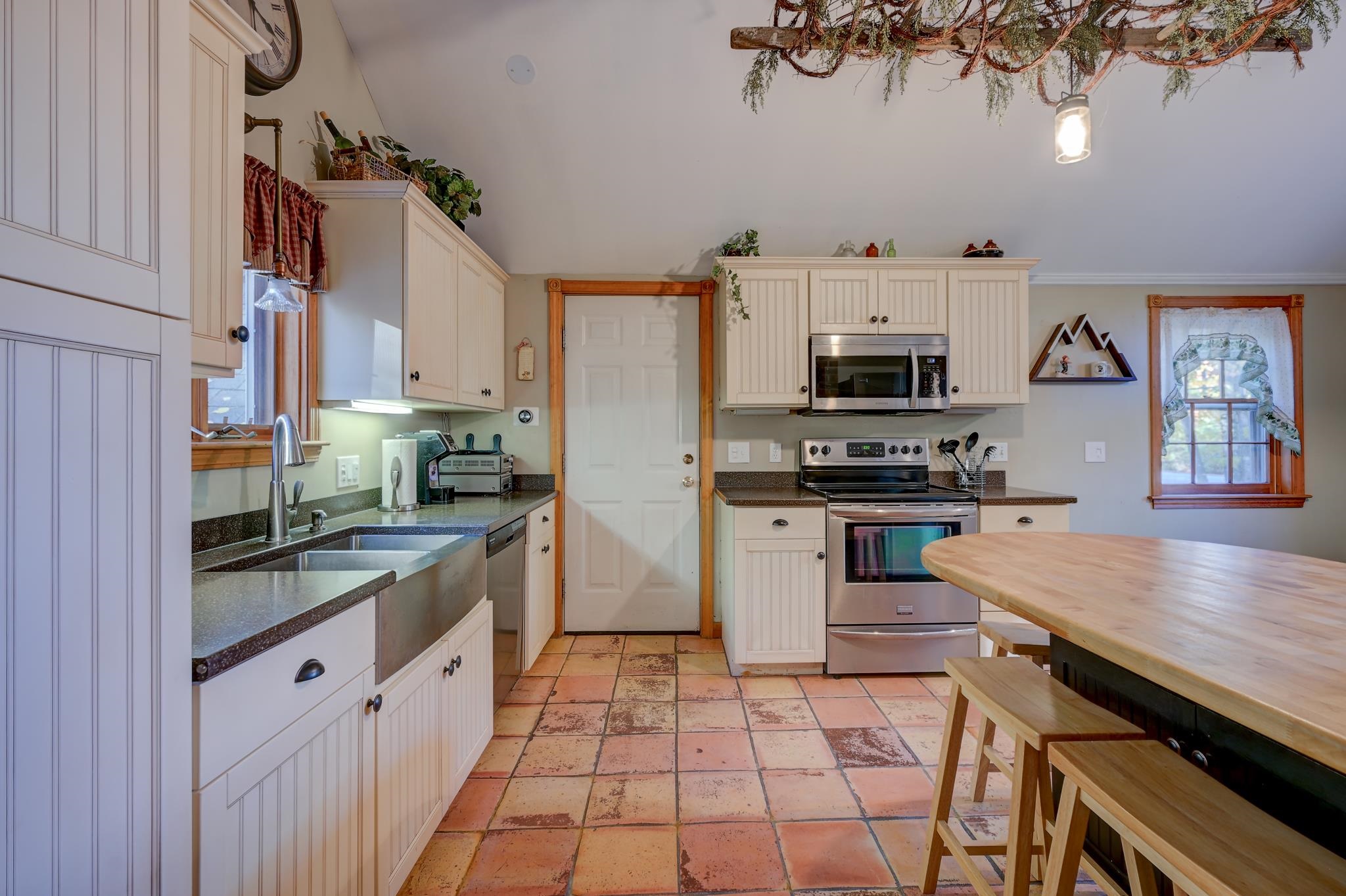Kitchen with cream cabinets, stainless steel appliances, terracotta tile, and a wooden island with stools.