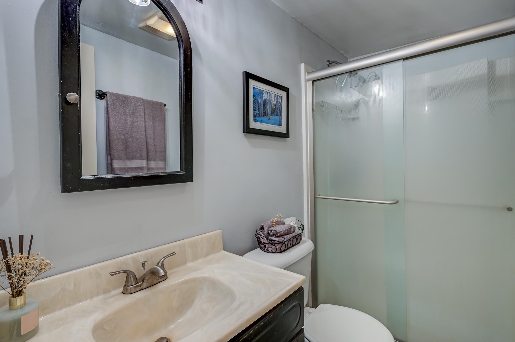 Bathroom with a cream stone vanity, black-framed mirror, and frosted-glass shower door.