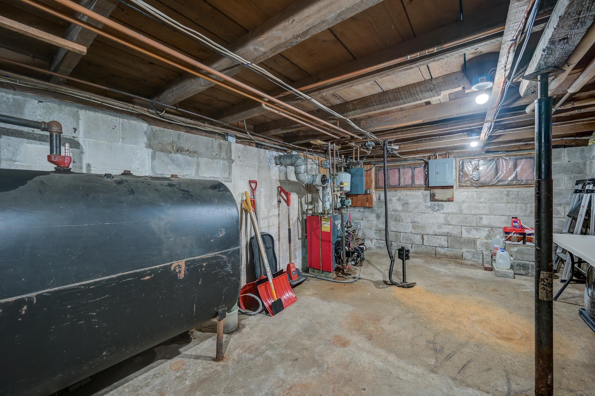 Basement utility room with a large oil tank, red boiler, exposed pipes, and concrete block walls.